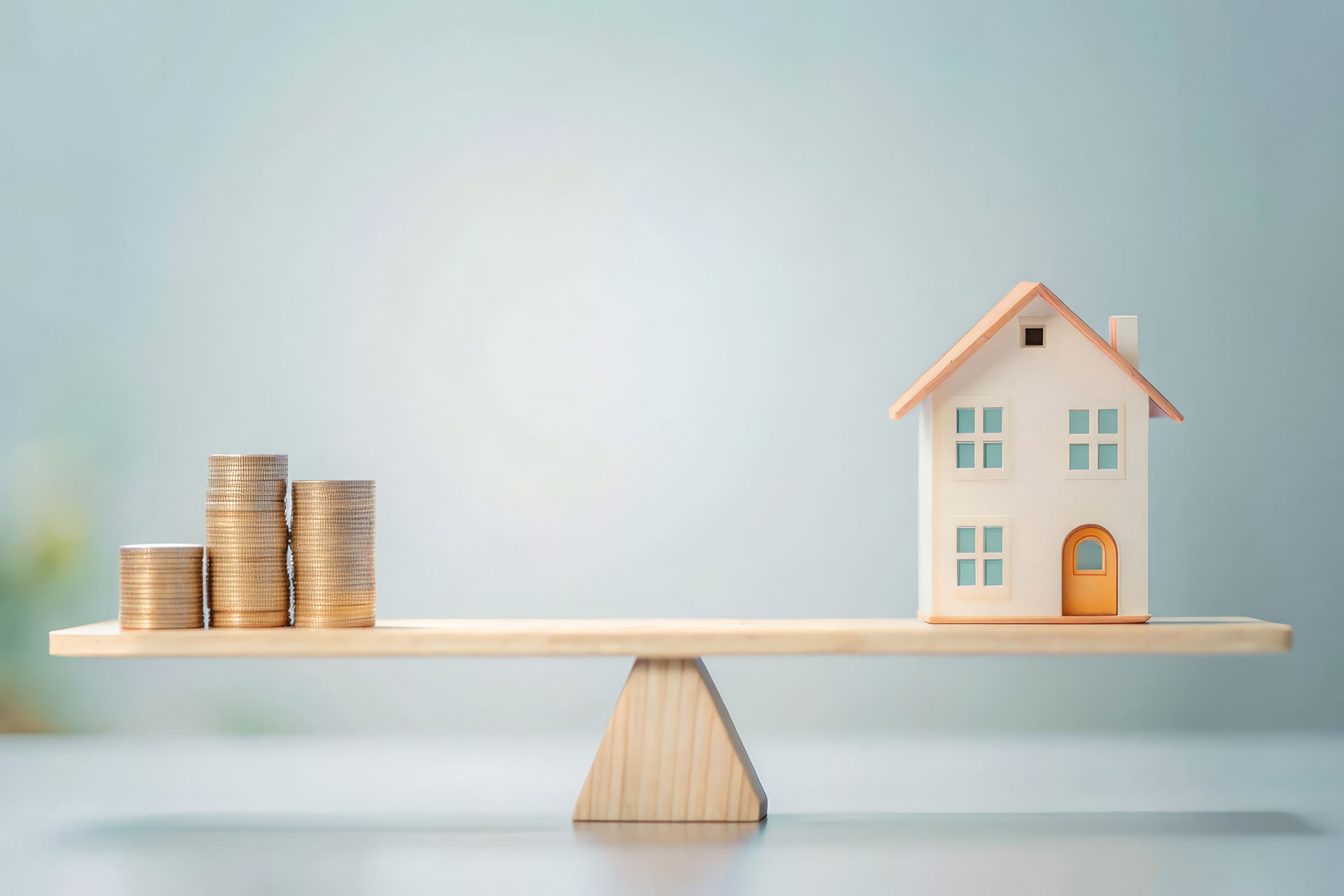 Modellhaus mit Münzen auf einer Holzwaage als Symbol für den Angebotspreis und Verkaufspreis
