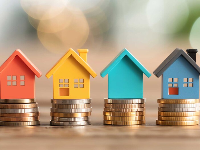 Modellhäuser auf Münzstapeln als Symbol für die Mietpreisgestaltung von Anlageimmobilien