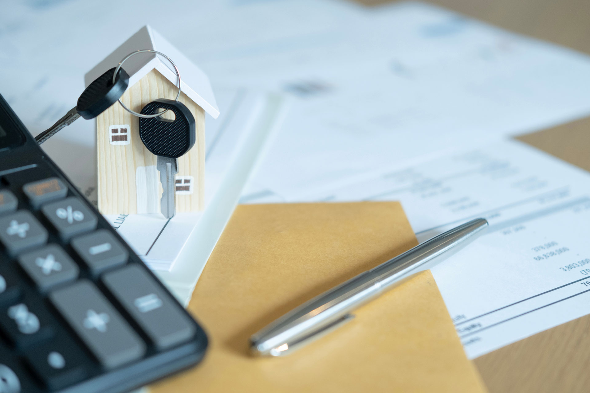 Taschenrechner, Modellhaus, Unterlagen und Schlüssel: Symbol für die Nebenkosten beim Hauskauf