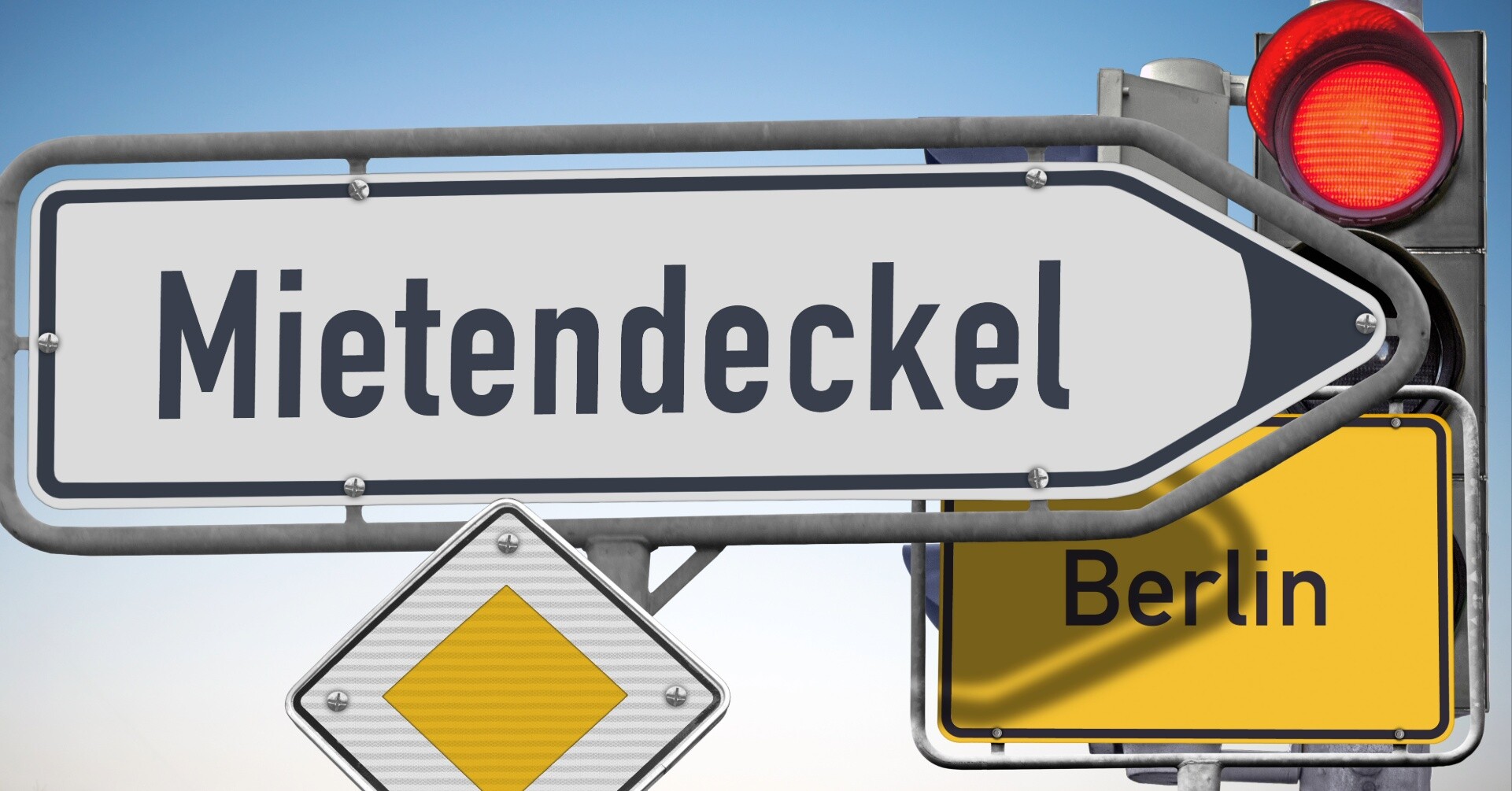 Ein Hinweisschild mit der Aufschrift Mietendeckel vor einem Ortsschild von Berlin und einer roten Ampel.