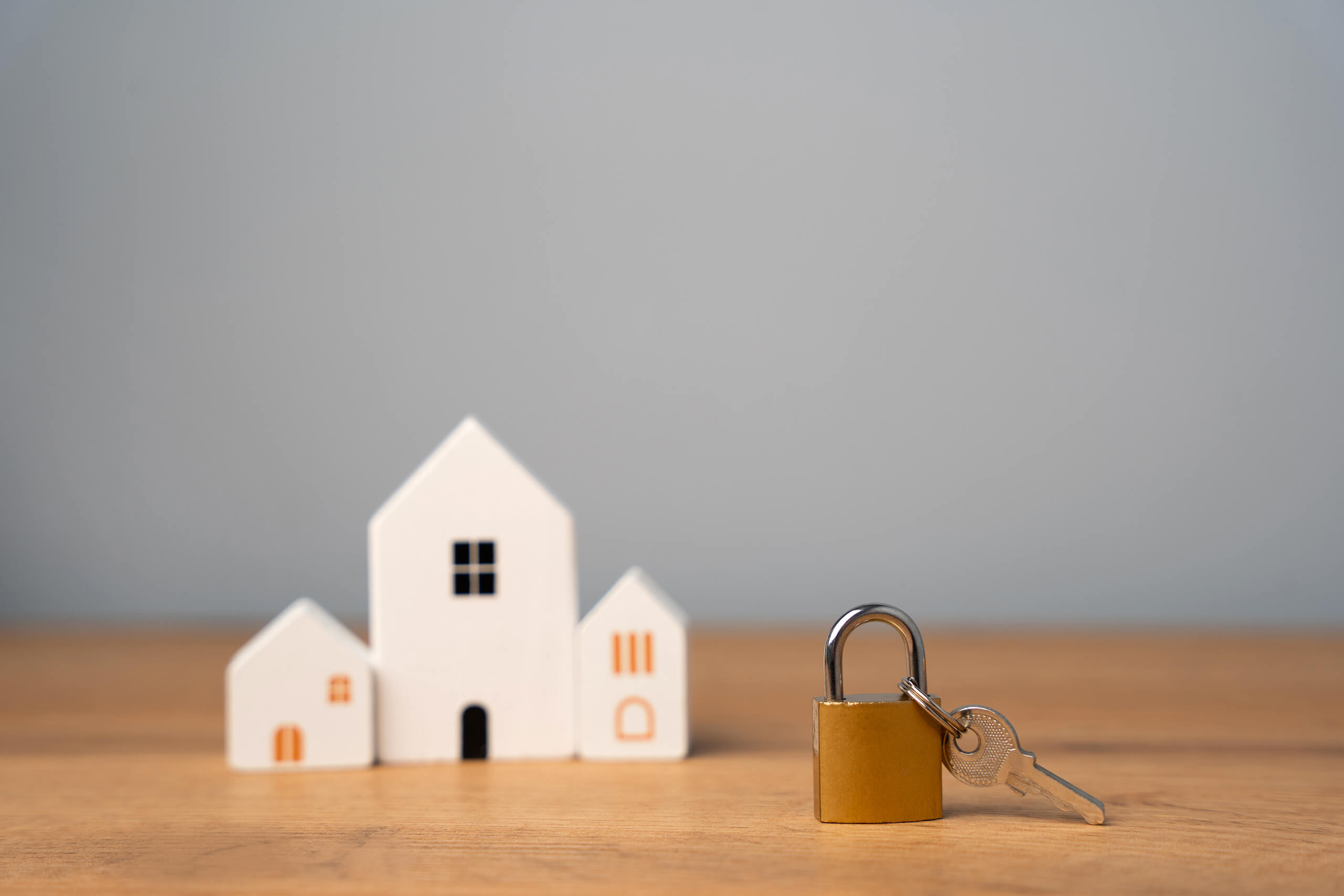 Vorhängeschloss mit Schlüsseln und Miniaturhäusern auf Holz.