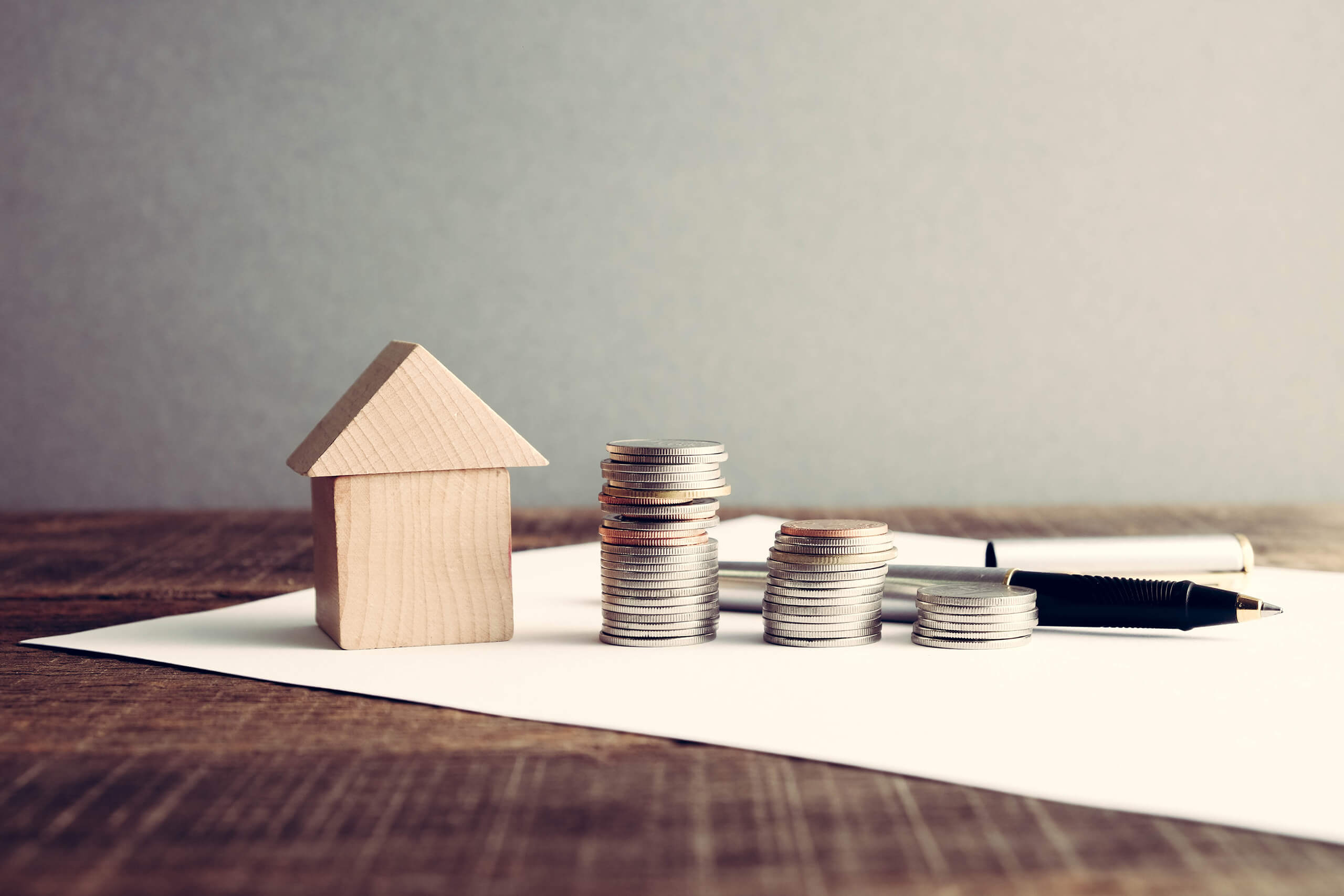 Holzhaus, Münzstapel und Stift auf Papier auf Holztisch.