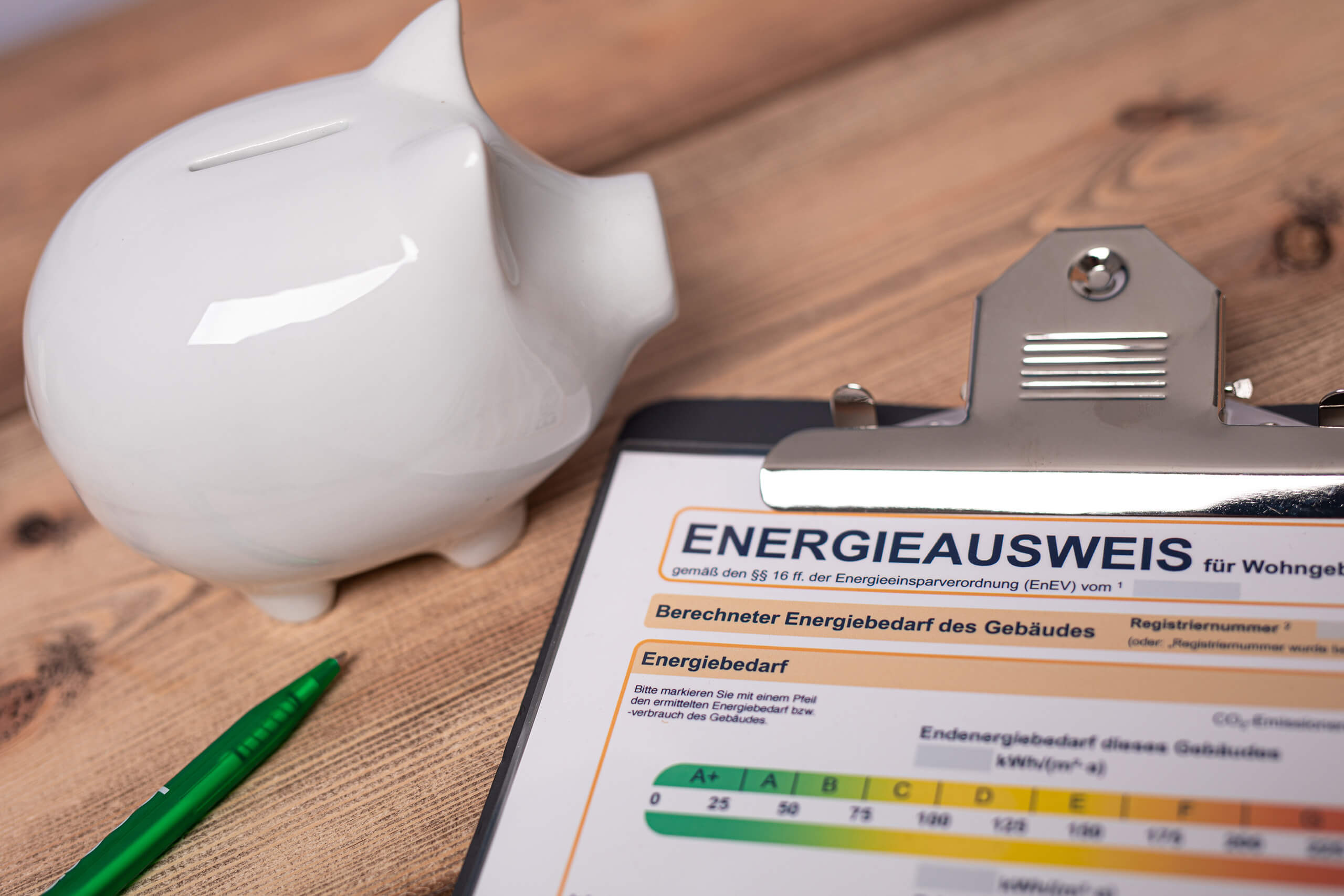 Sparschwein, grüner Stift und Formular auf Clipboard auf Holztisch.