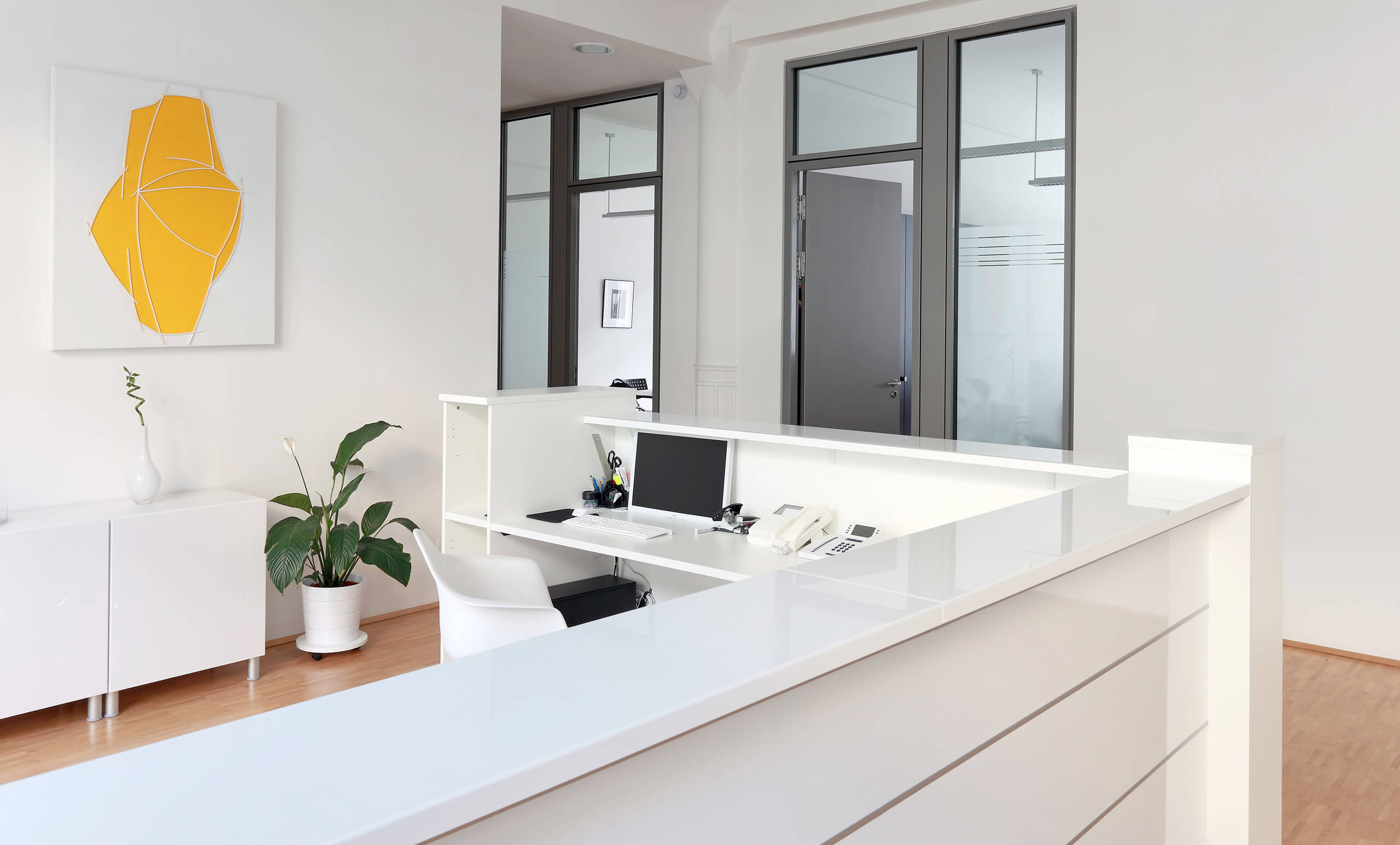 Moderne Rezeption mit weißen Möbeln, Schreibtisch, Pflanze, Kunst.