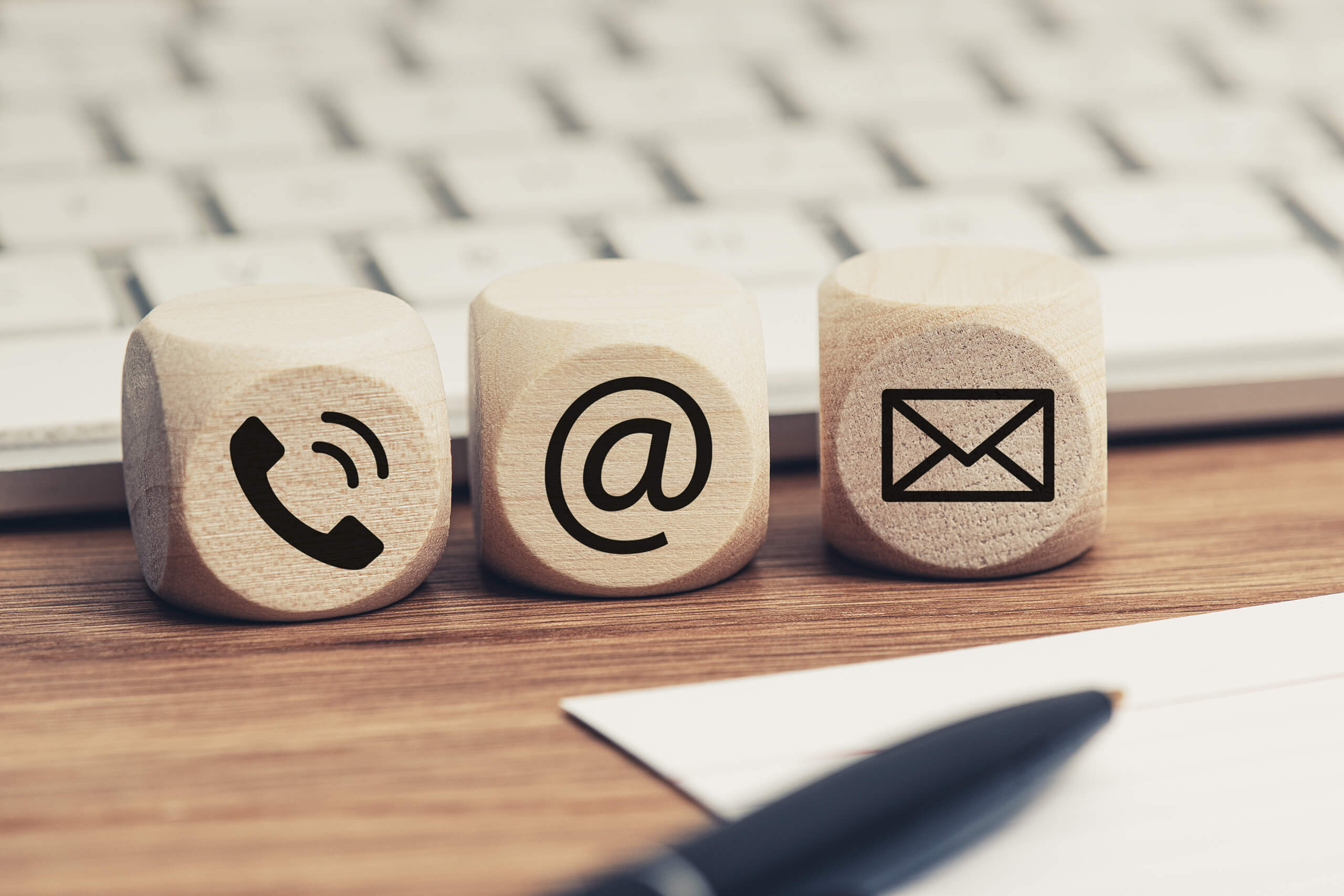 Holzblöcke mit Telefon-, E-Mail- und Briefsymbol vor Tastatur.