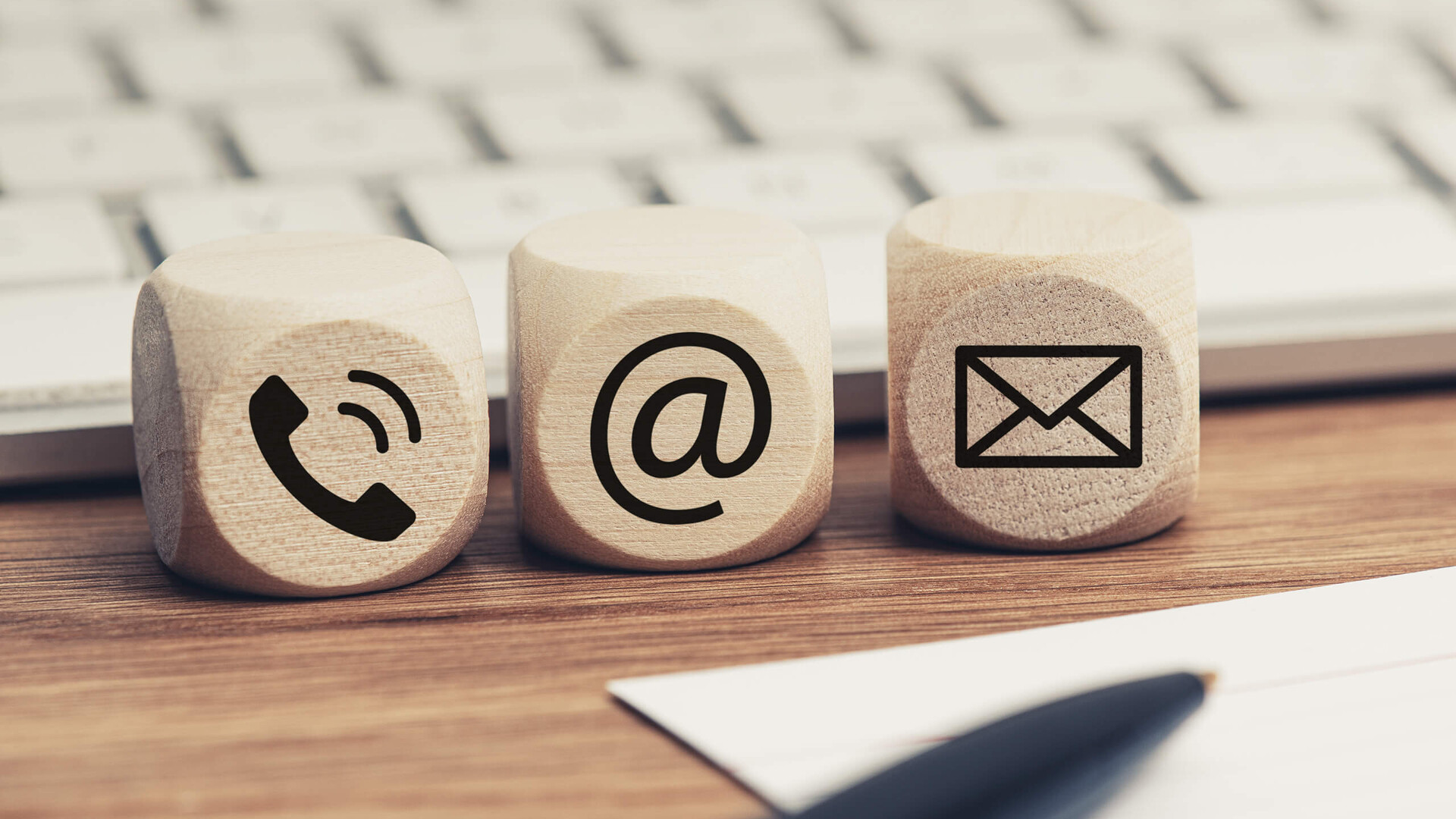 Holzblöcke mit Telefon-, E-Mail- und Briefsymbol vor Tastatur.