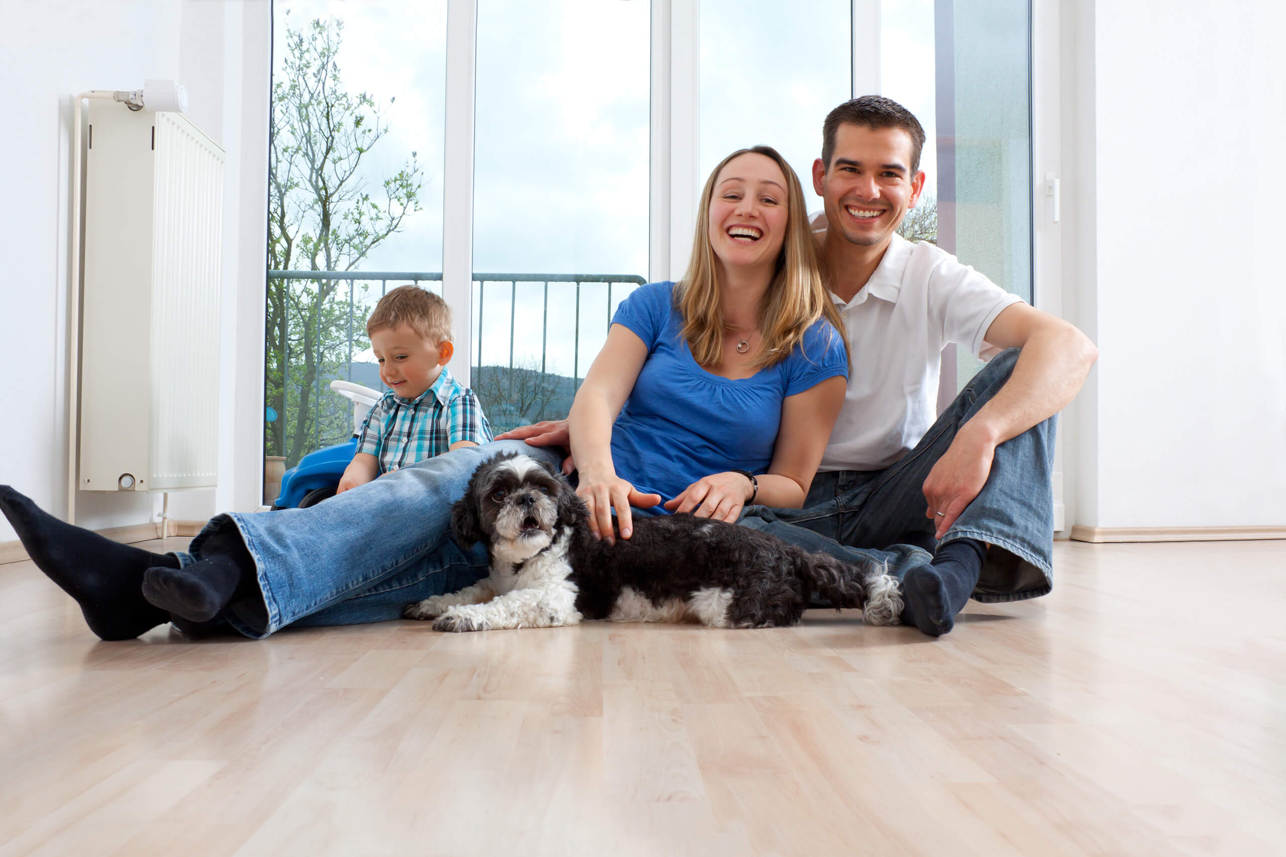 Paar mit Hund am Boden, Junge spielt im hellen Zimmer.