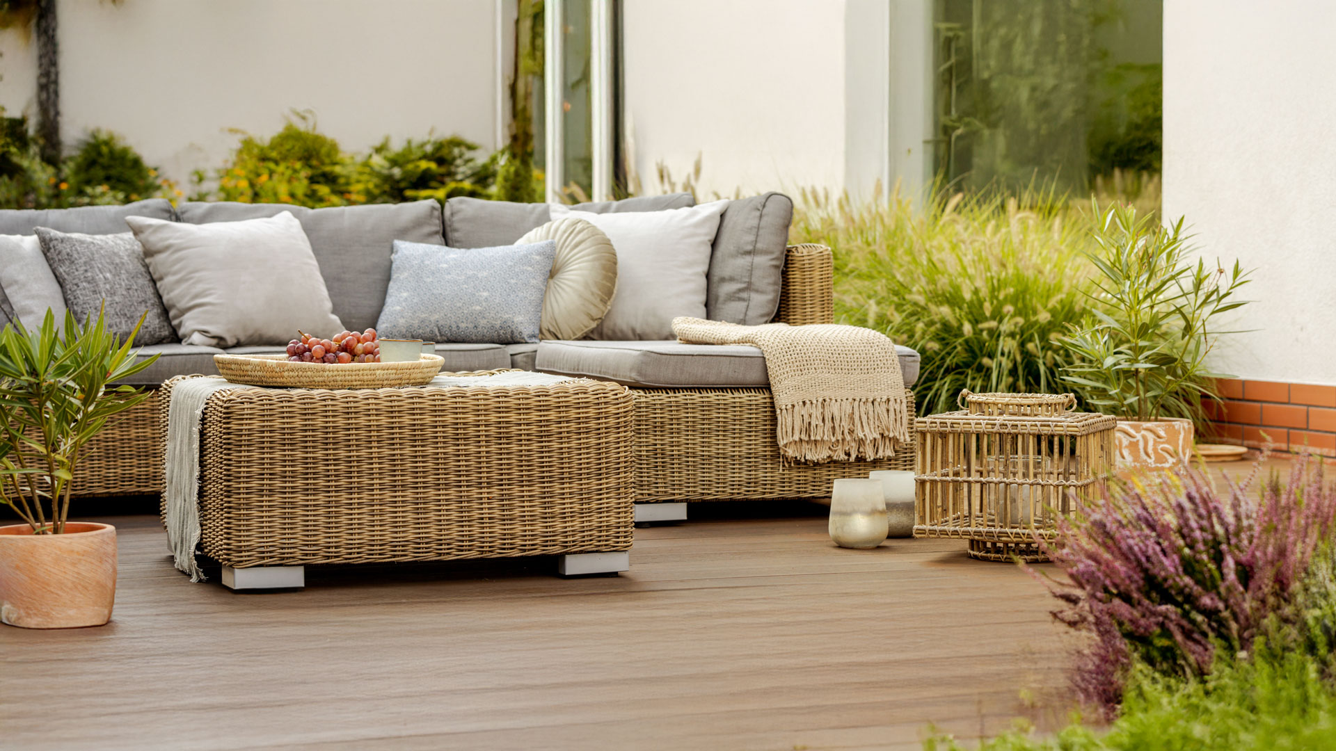 Wicker Sofa und Tisch mit Kissen auf Holzdeck, von Pflanzen umgeben.