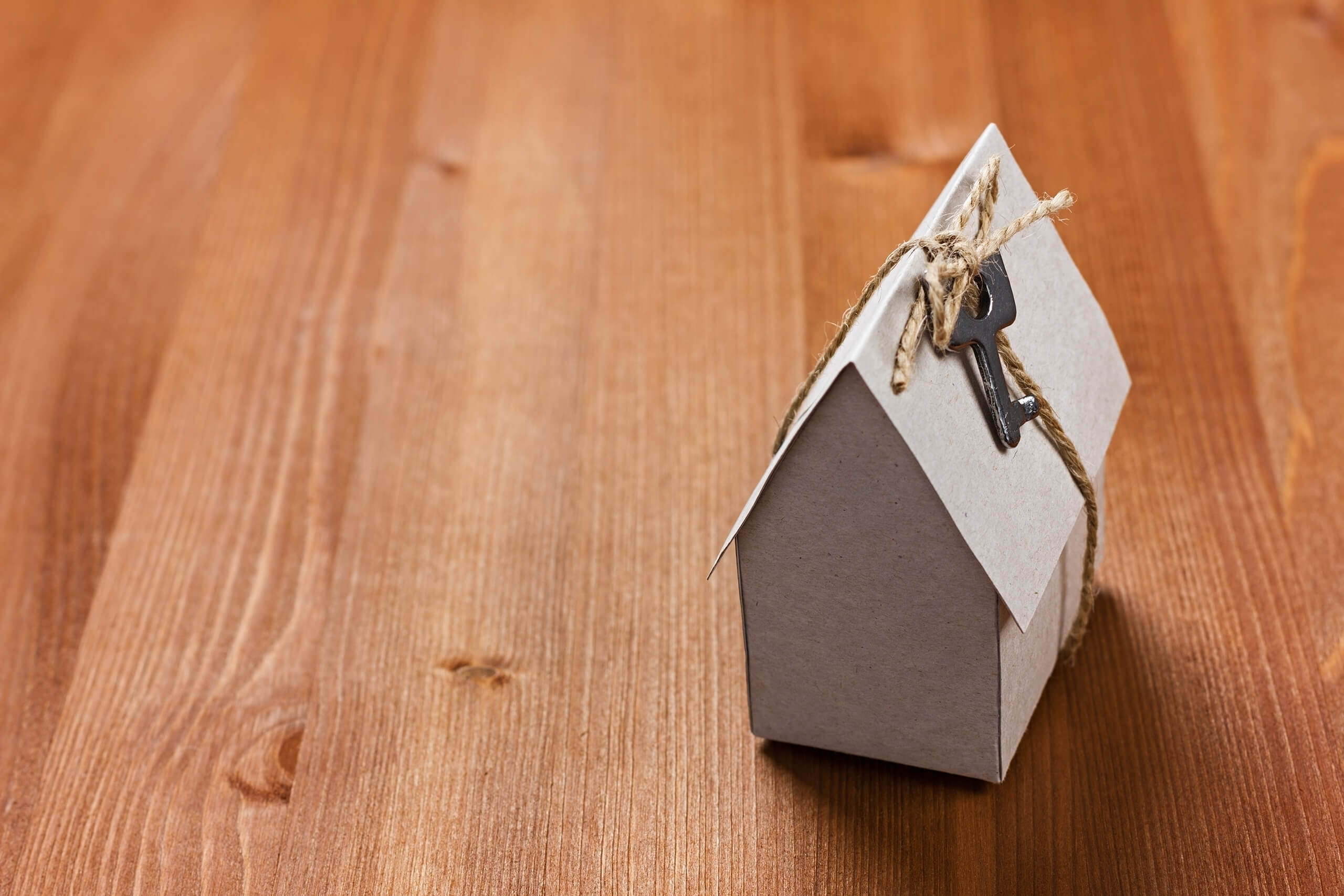 Kartonhaus mit Schlüssel auf Holzoberfläche.