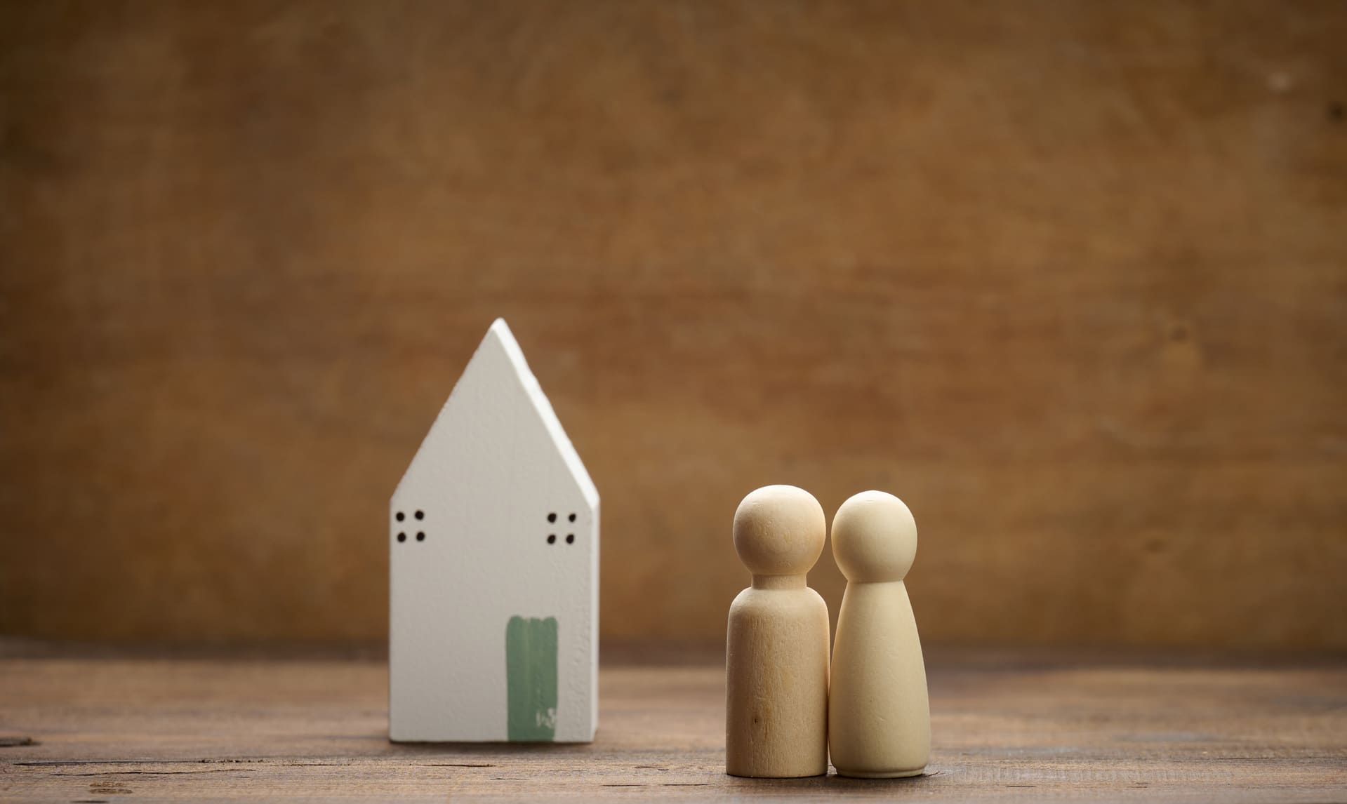 Miniaturfiguren einer Familie neben einem Modellhaus auf braunem Hintergrund.