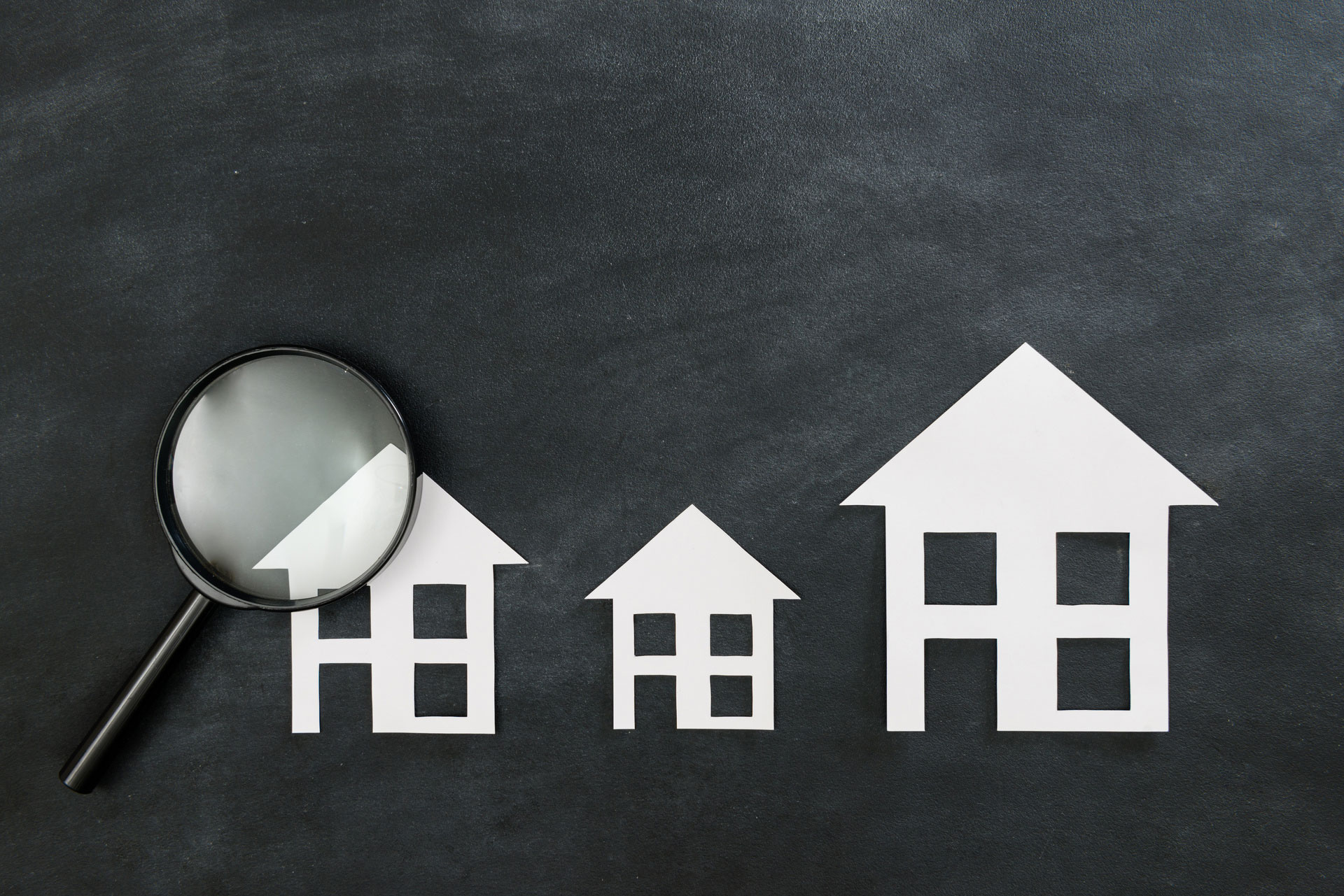 Papierhäuser und Lupe vor dunklem Hintergrund