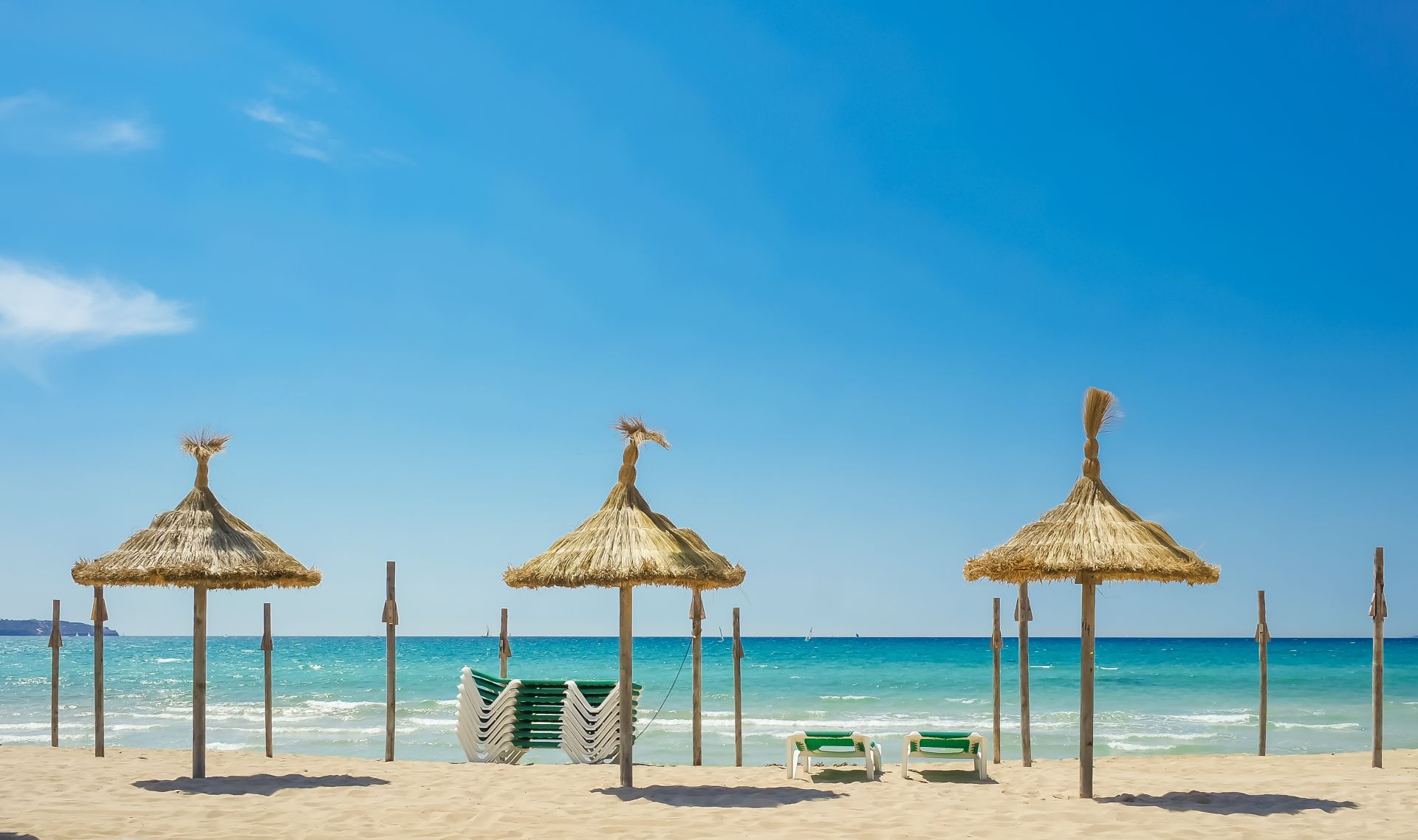 Strohsonnenschirme und Liegen am Strand vor türkisfarbenem Meer.