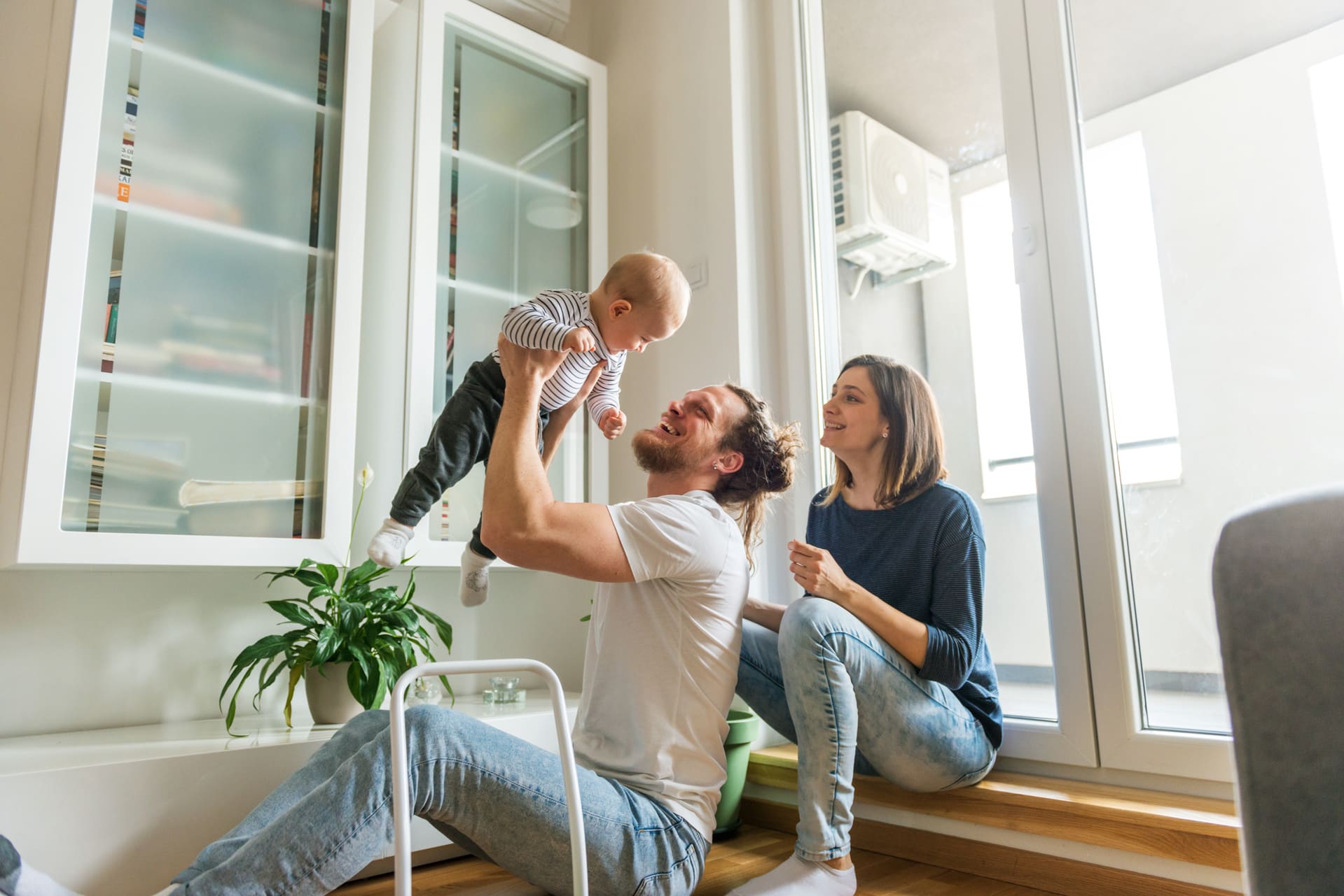 Junge Eltern spielen gemeinsam mit ihrem Baby im Wohnzimmer.