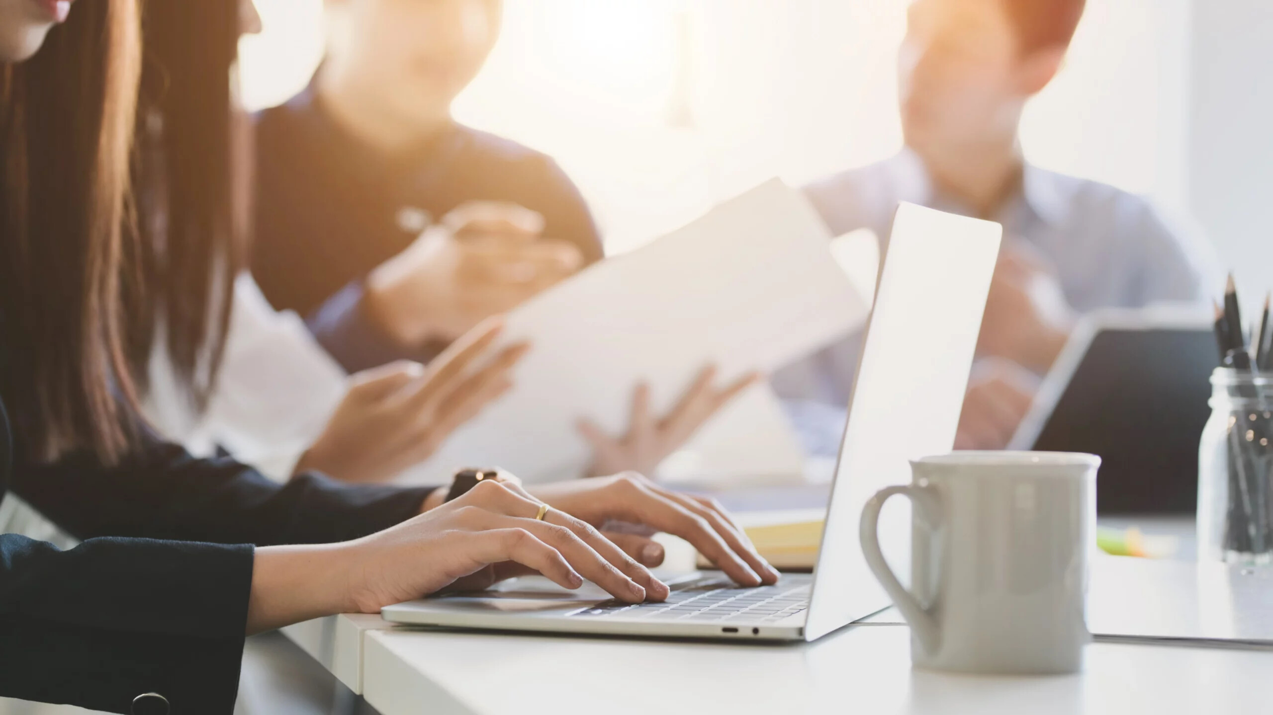 Nahaufnahme von mehreren Personen, die gemeinsam mit Laptops am Tisch zusammenarbeiten.