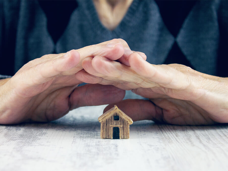 Mann hält Hände schützend über Mini-Haus