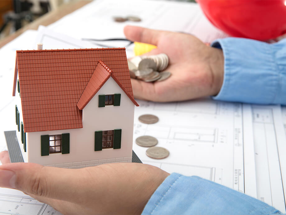 Mann hält Münzen und Hausmodell in Händen
