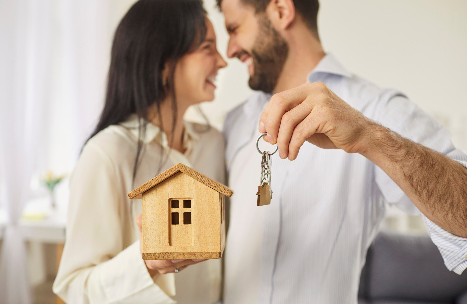 Glückliches Paar hält Schlüssel und Hausmodell in Händen