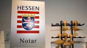 Schild mit dem hessischen Wappen und dem Wort Notar neben einem Gestell mit mehreren Notarstempeln.