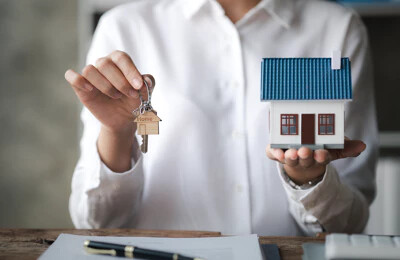 Frau hält kleines Haus und Schlüssel