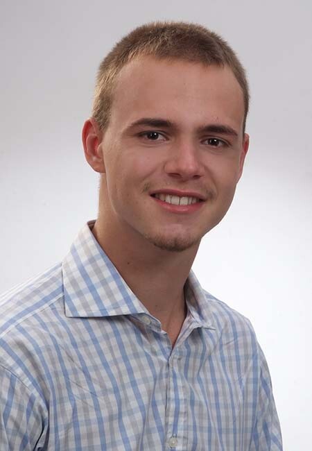 Junger Mann mit kurzem Haar im karierten Hemd, lächelt.