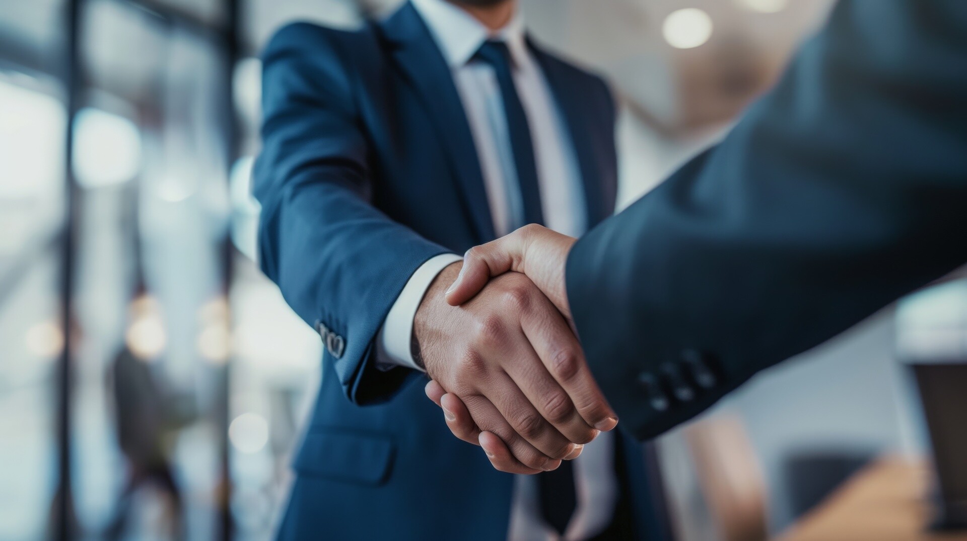 Zwei Menschen im Anzug schütteln sich im Büro die Hand.