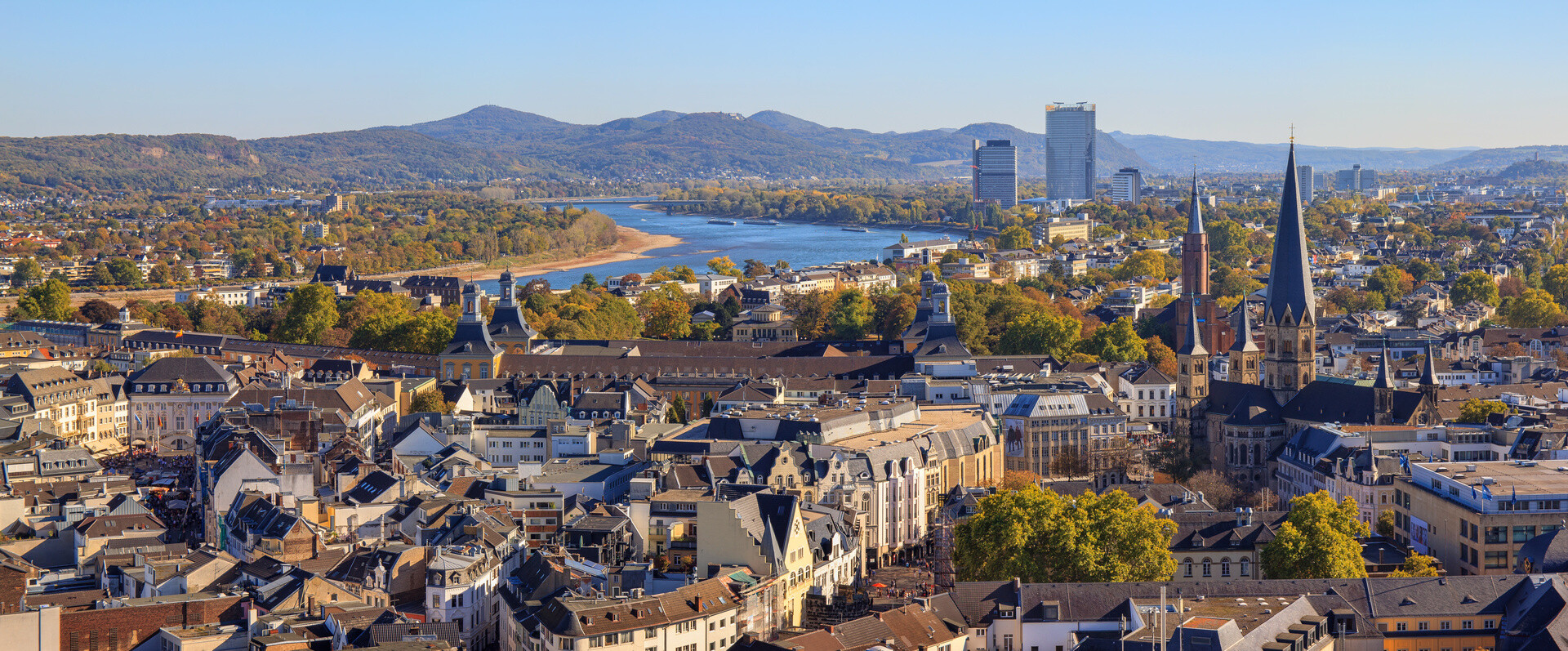 Bonn am Rhein mit Altbauten und Hügeln unter klarem Himmel.