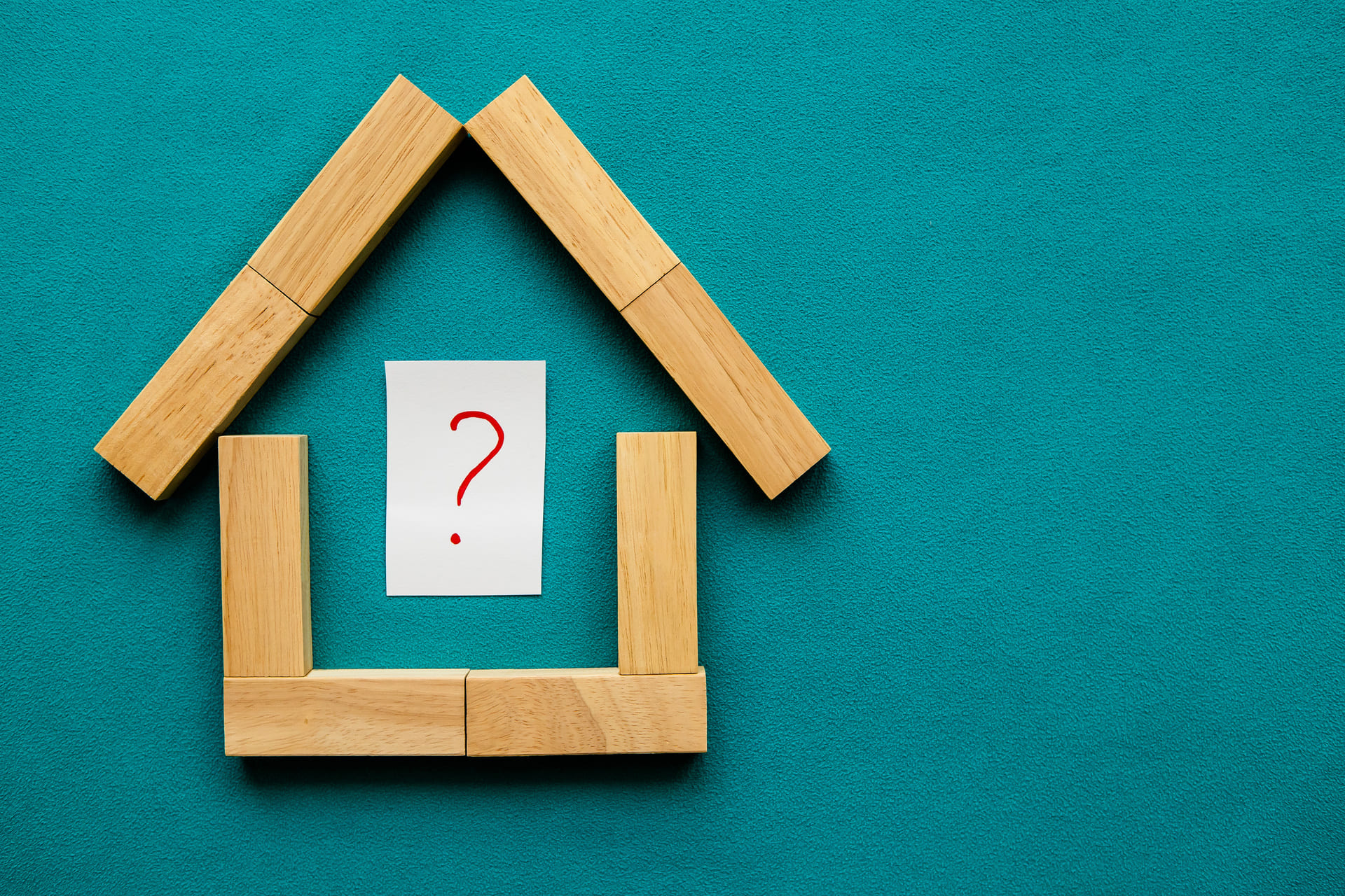 Wichtige Punkte vor dem Hauskauf visualisiert durch Holzhaus und rotes Fragezeichen.