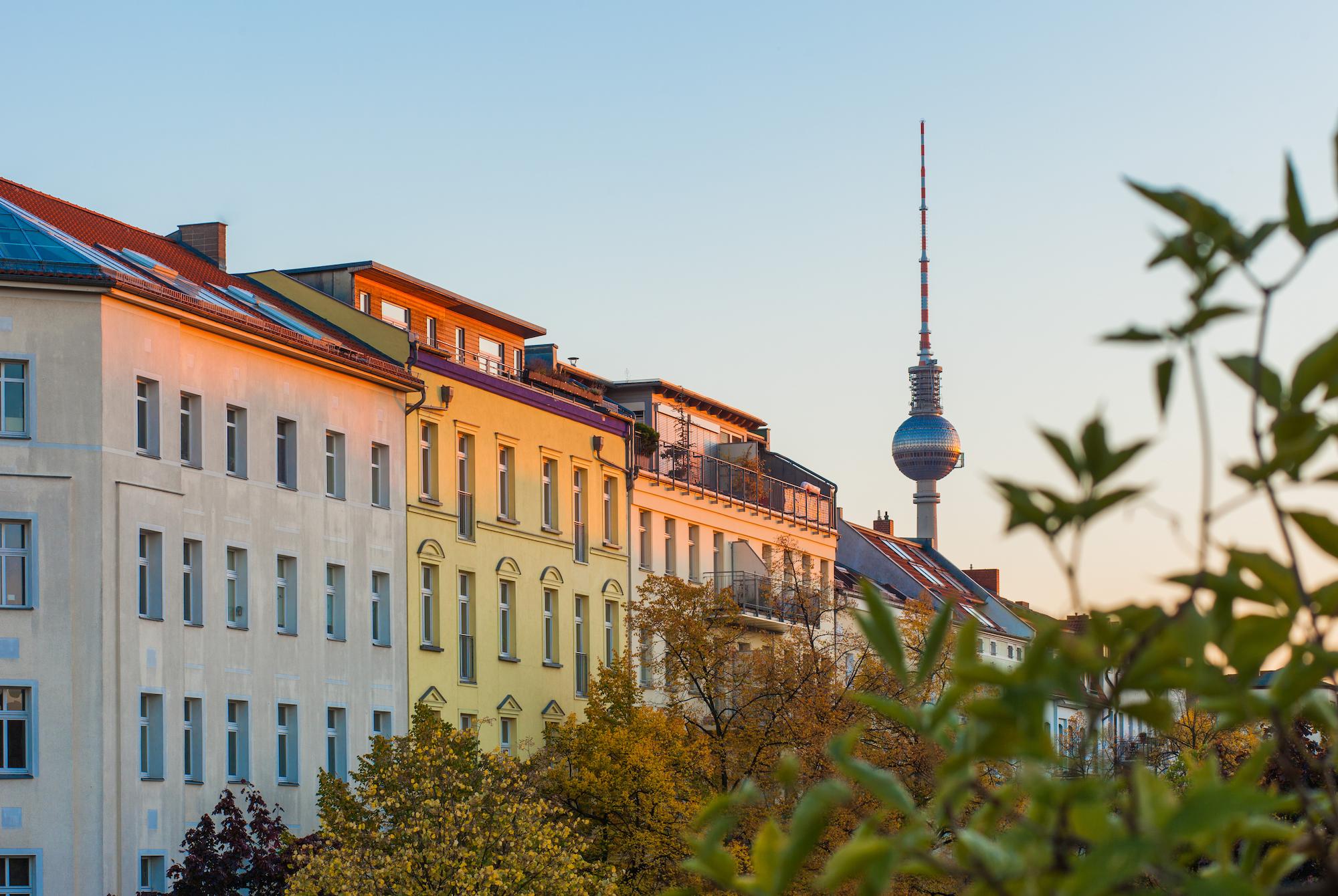Bunte Wohnhäuser mit Berliner Fernsehturm bei Sonnenuntergang.