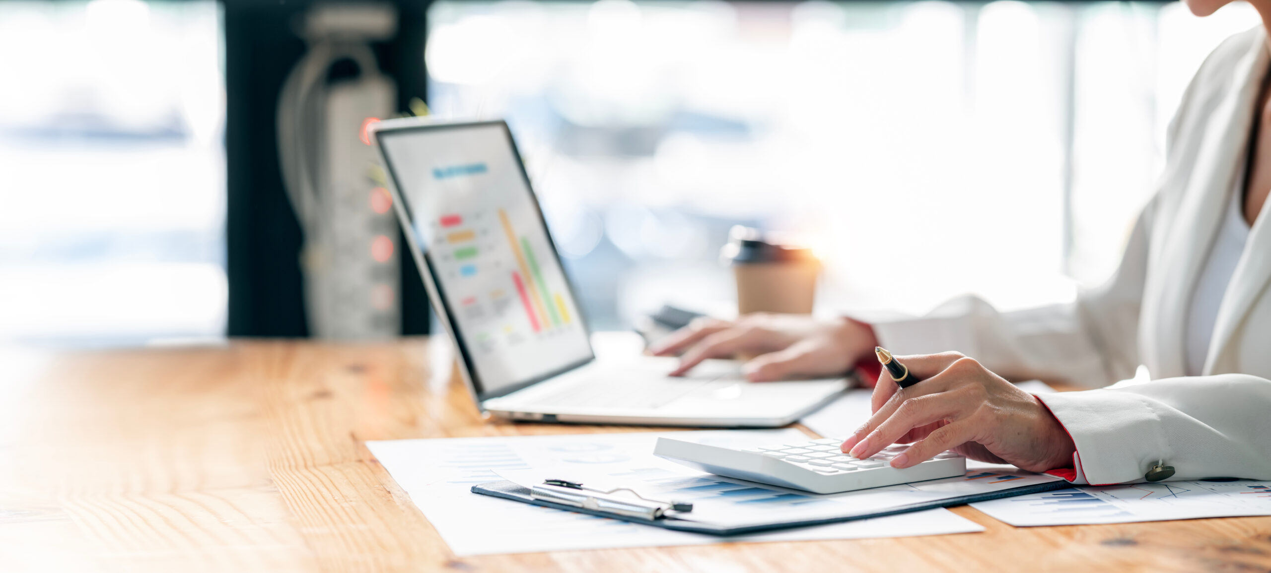Person mit Taschenrechner und Laptop mit Finanztabellen in der Nähe.