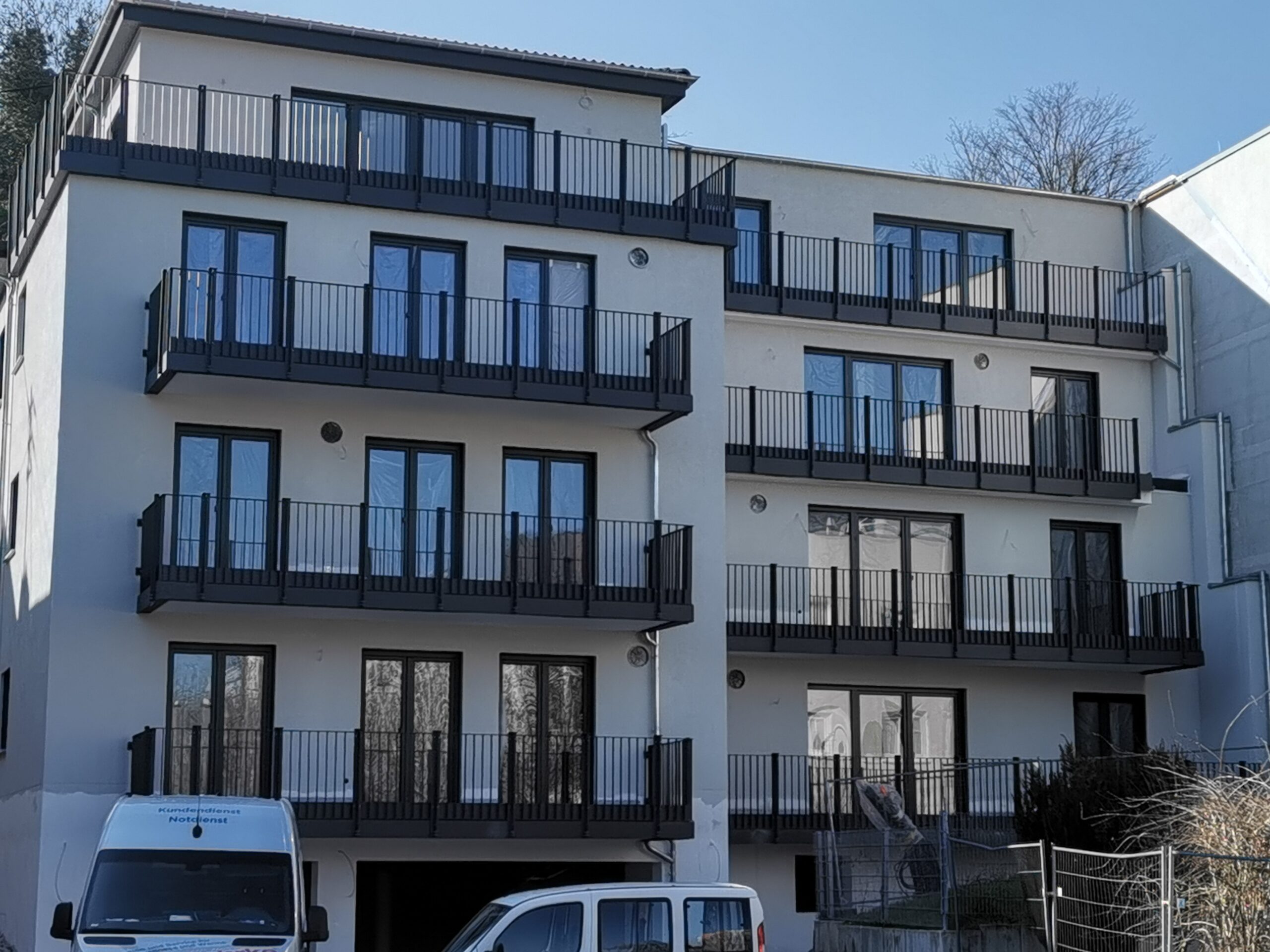 Vierstöckiges Apartmenthaus mit Balkonen und zwei weißen Vans davor.