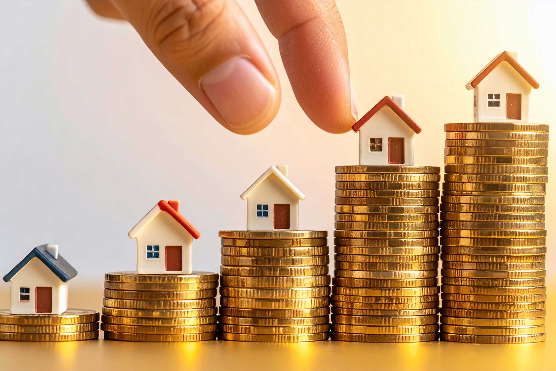 Modellhäuser auf verschieden großen Münzstapeln, Symbol für Immobilienpreise