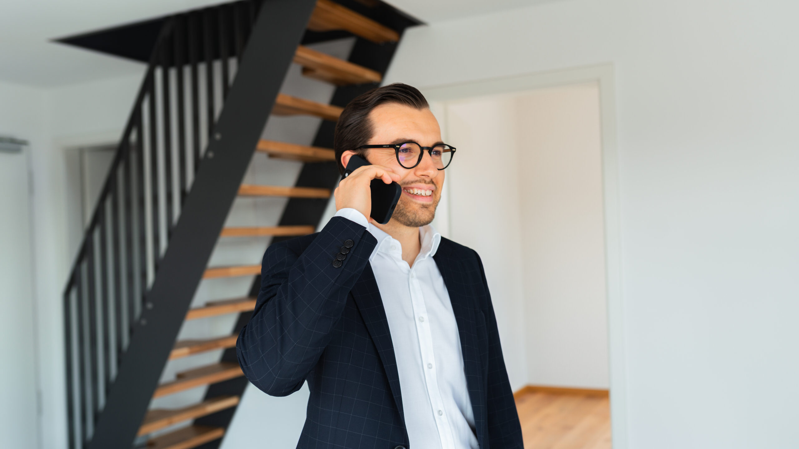 Mann lächelnd steht vor Treppe und ist am telefonieren mit einem Kunden.