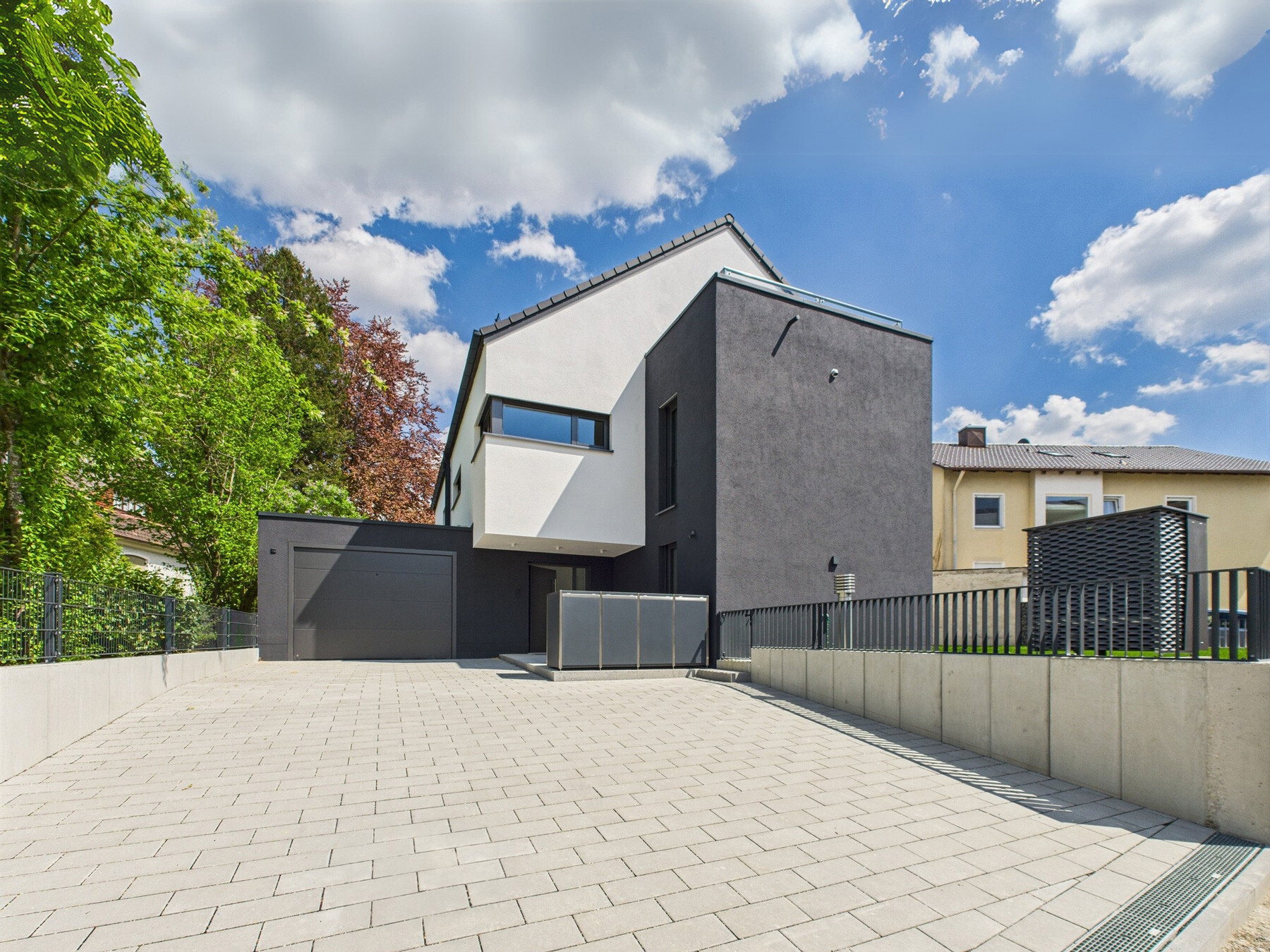 Modernes Haus mit Flachdach und großer Einfahrt bei Wolken.