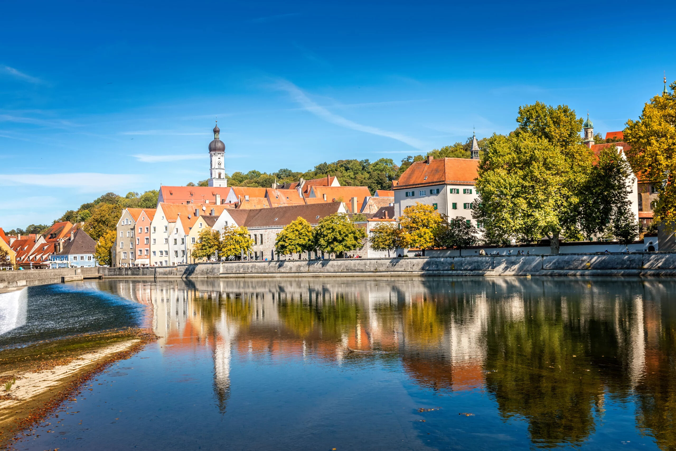 Bunte Häuser mit roten Dächern und Kirche spiegeln sich im Fluss.