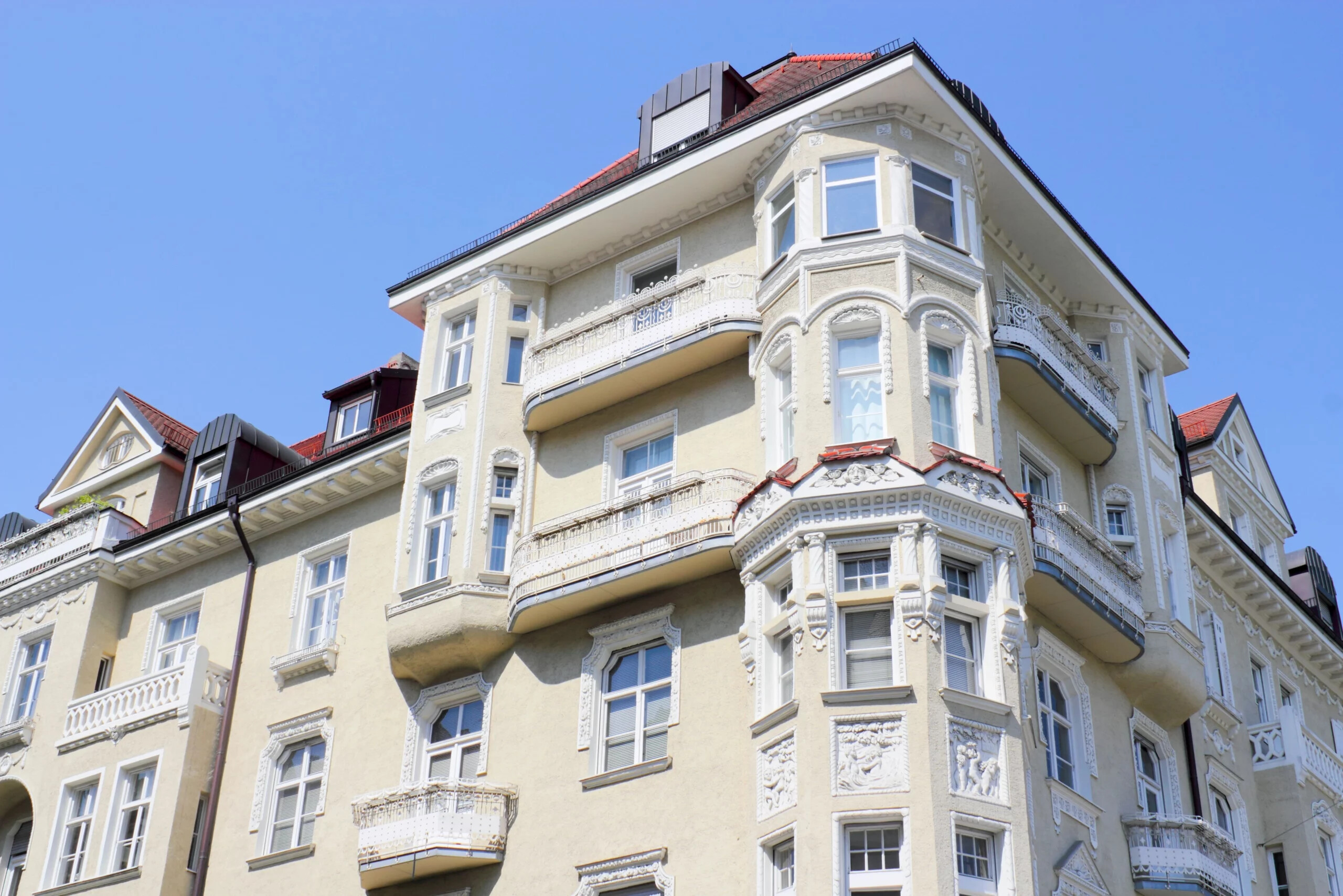 Helles Apartmenthaus mit Balkonen und Schnitzereien bei blauem Himmel.