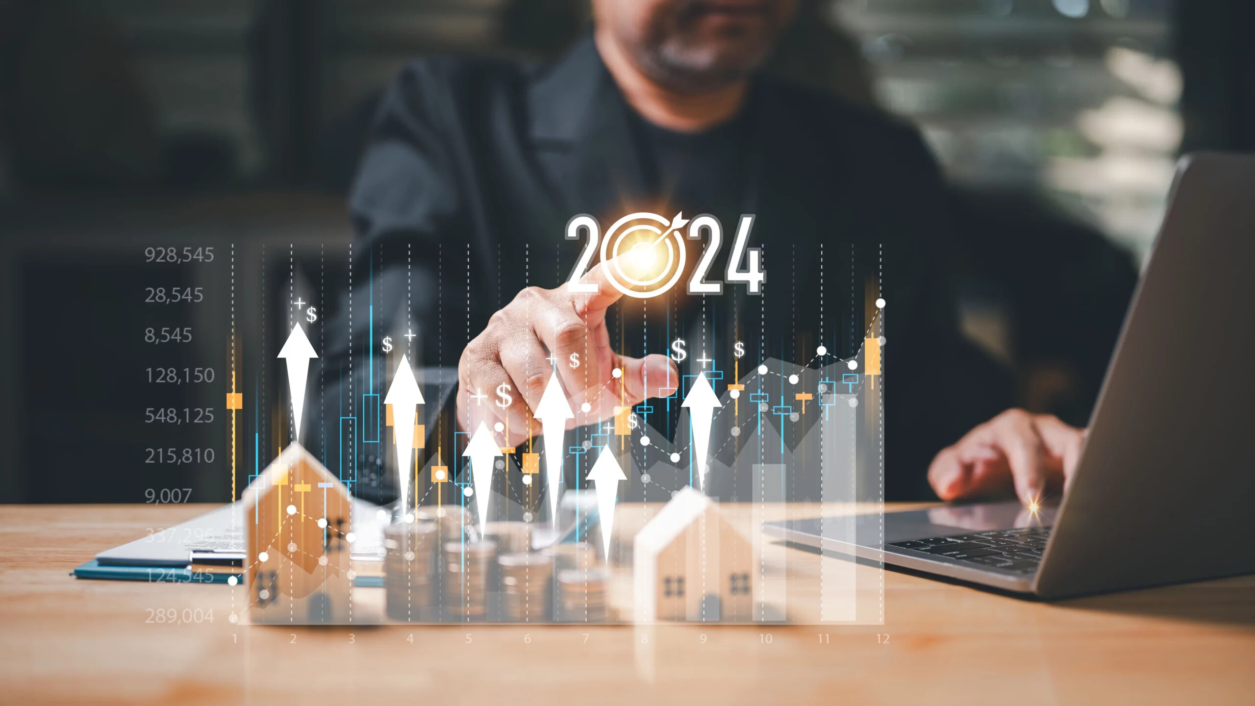Person zeigt auf 2024-Grafik mit Finanzdiagrammen und Hausmodellen.