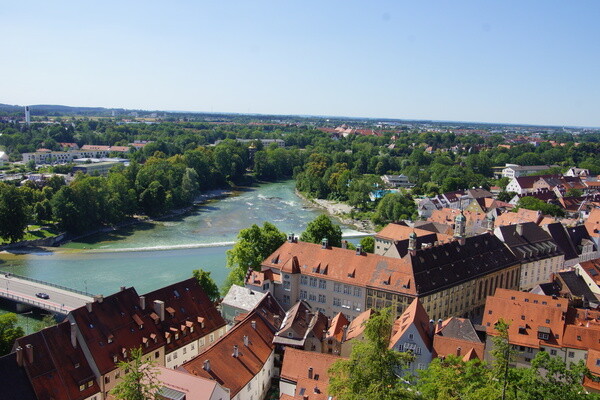Der Fluss fließt unter blauem Himmel an rotgedeckten Gebäuden und Bäumen vorbei.