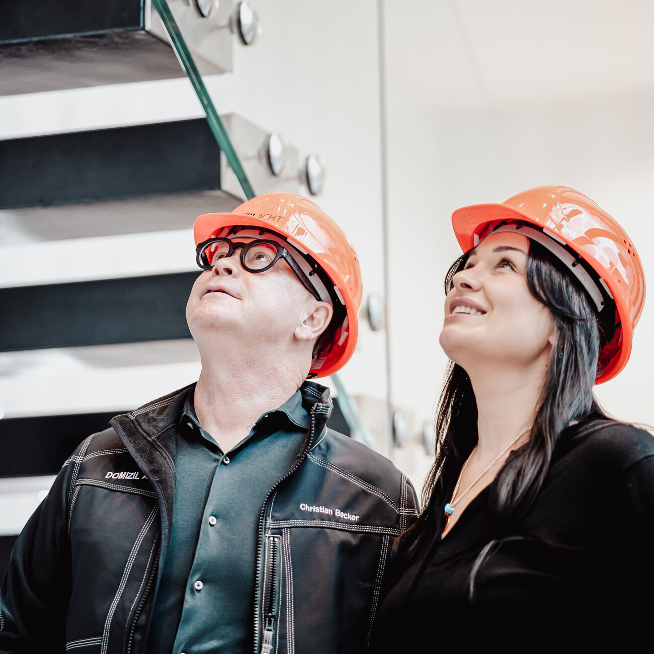 Zwei Personen mit orangefarbenen Helmen schauen nach oben drinnen.