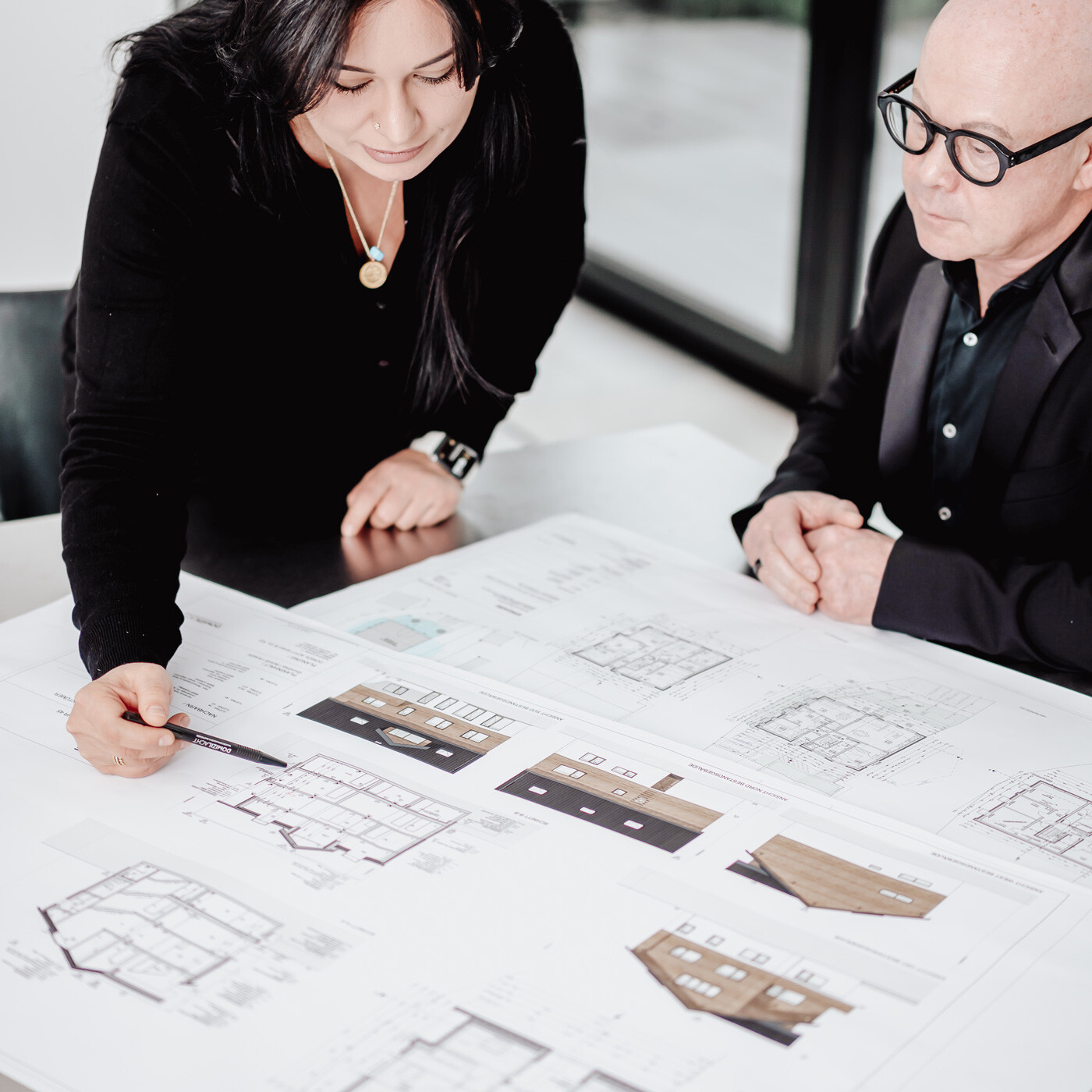 Zwei Personen betrachten Baupläne und Hausentwürfe am Tisch.