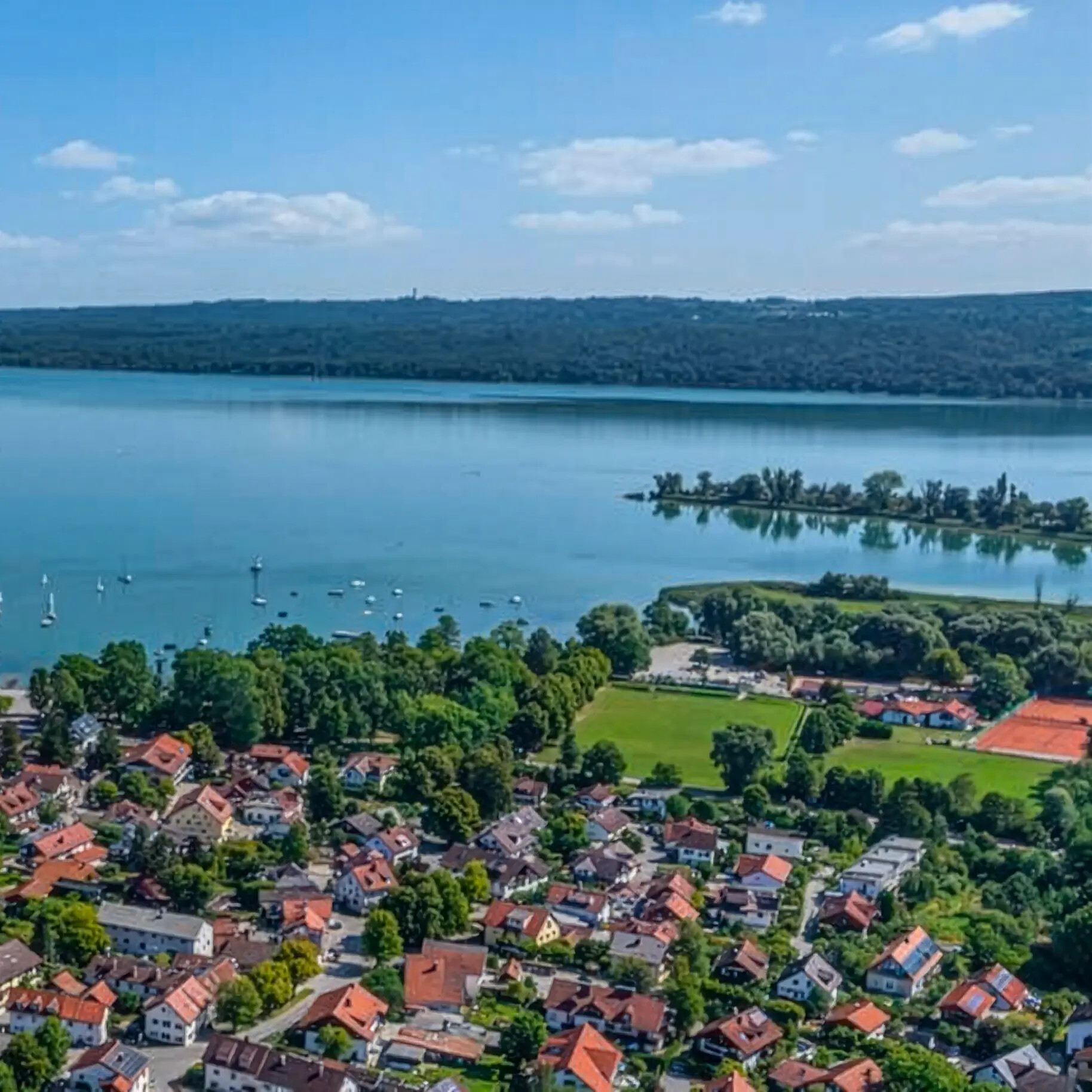 Diessen am Ammersee mit Häusern, Booten, Grünanlagen und blauem Wasser.