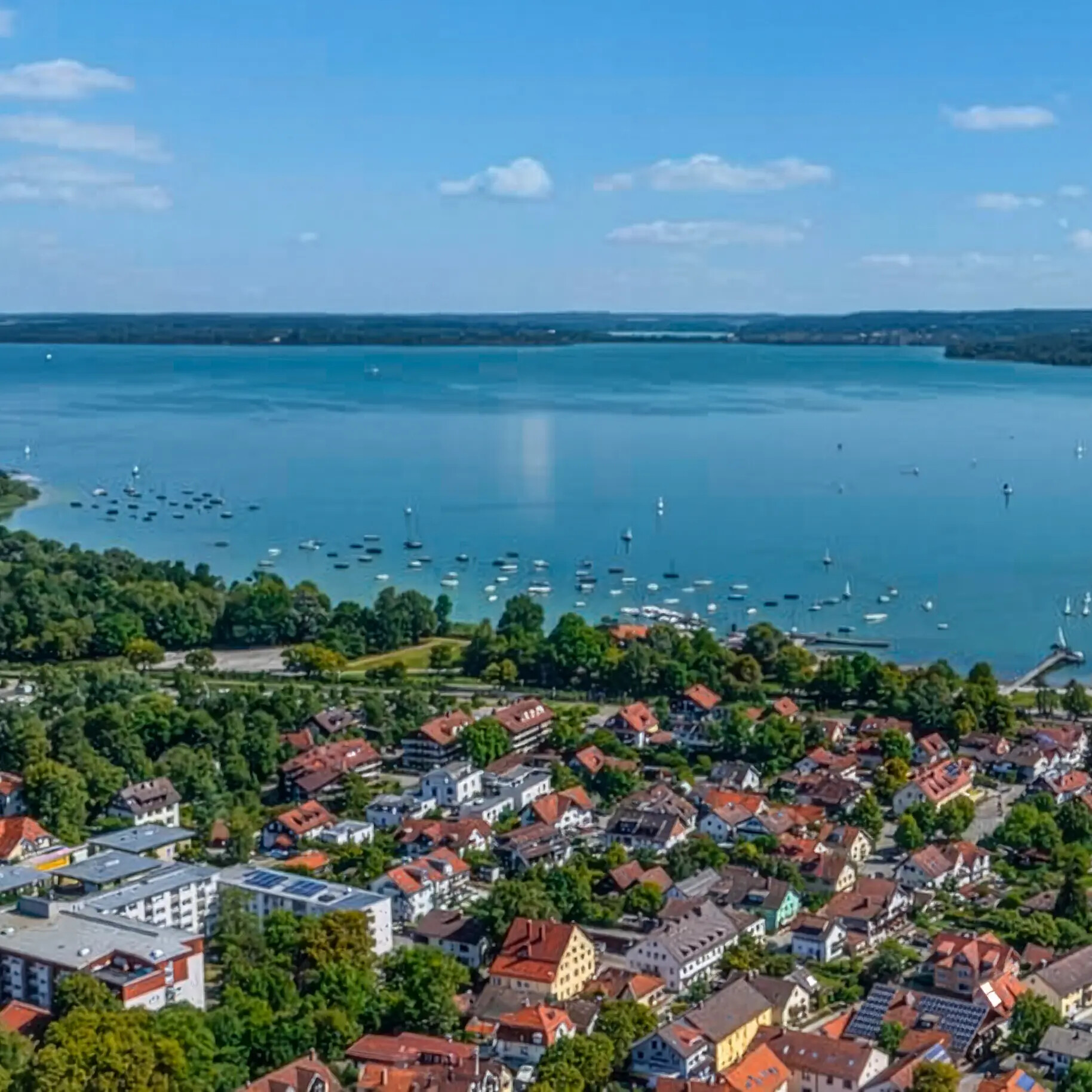 Diessen am Ammersee mit Häusern, Booten, Grünanlagen und blauem Wasser.