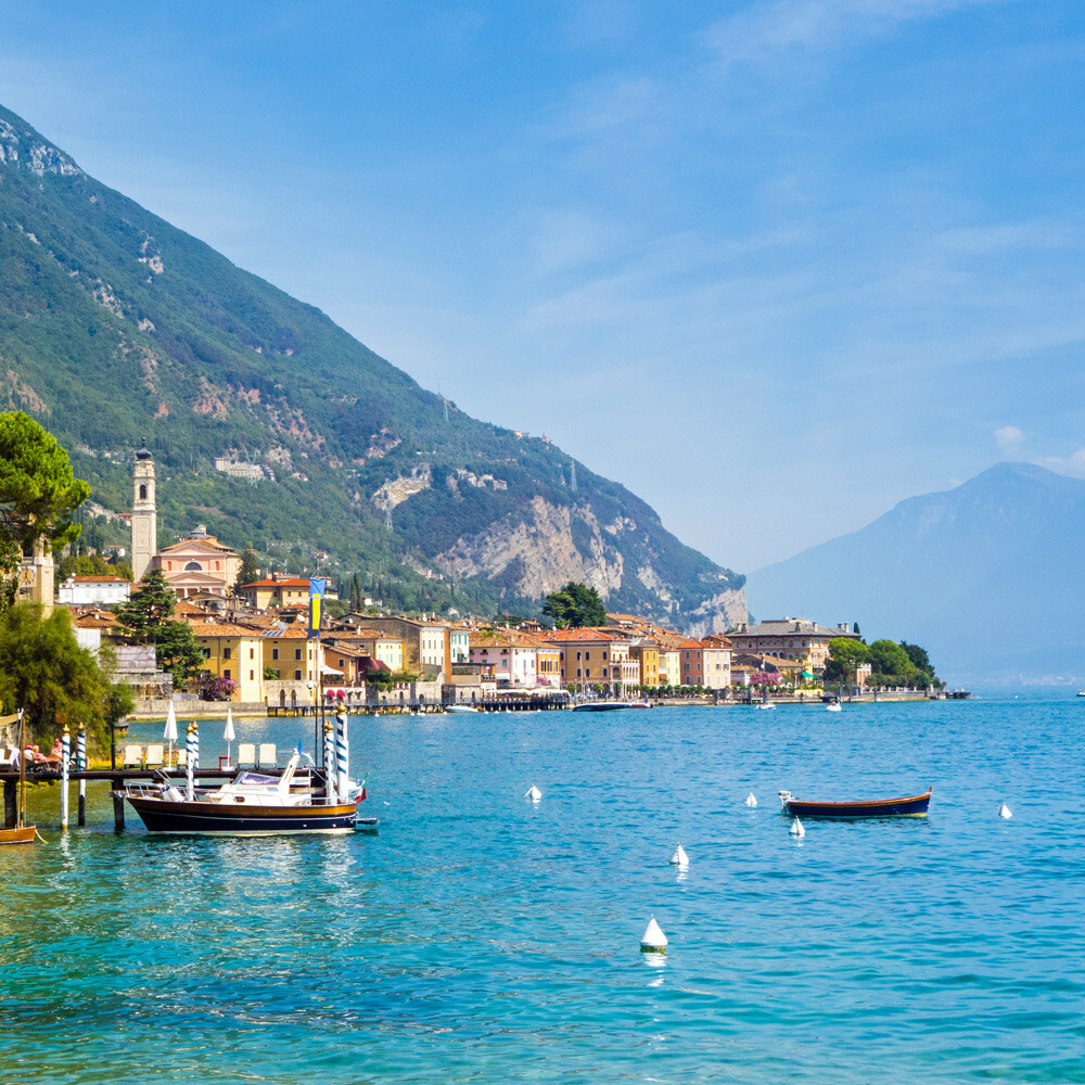 Blick auf eine Stadt am Ufer des Gardasee mit Booten und Gebirge