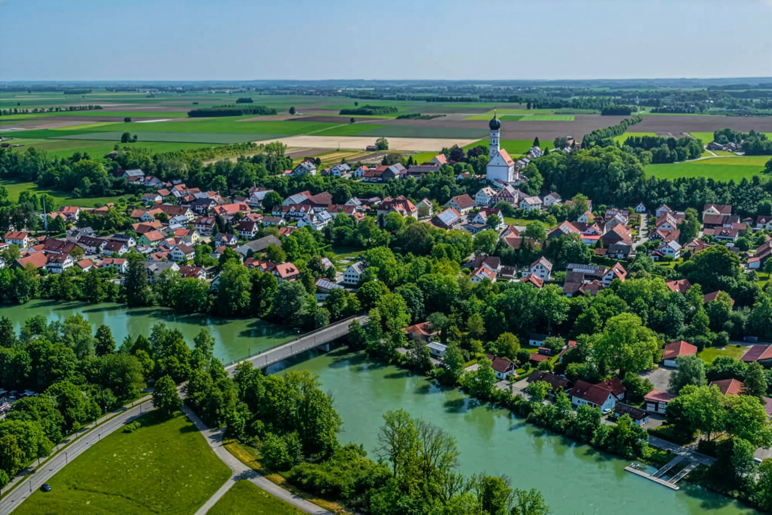 Stadt Kaufering mit roten Dächern, Kirche, Bäumen und Fluss aus der Luft.