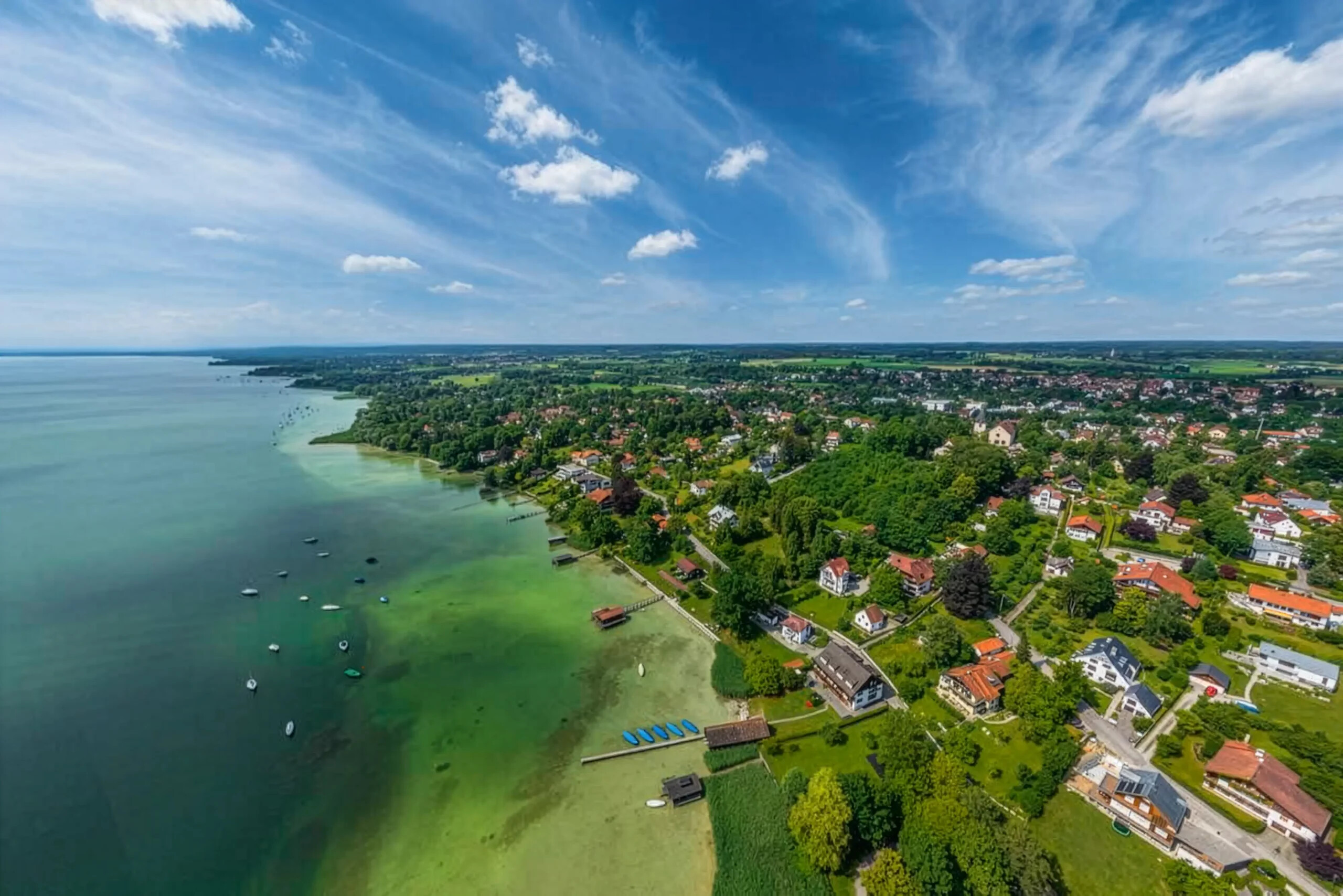Schondorf am Ammersee, grüne Bäume, Häuser, Boote auf blau-grünem Wasser.