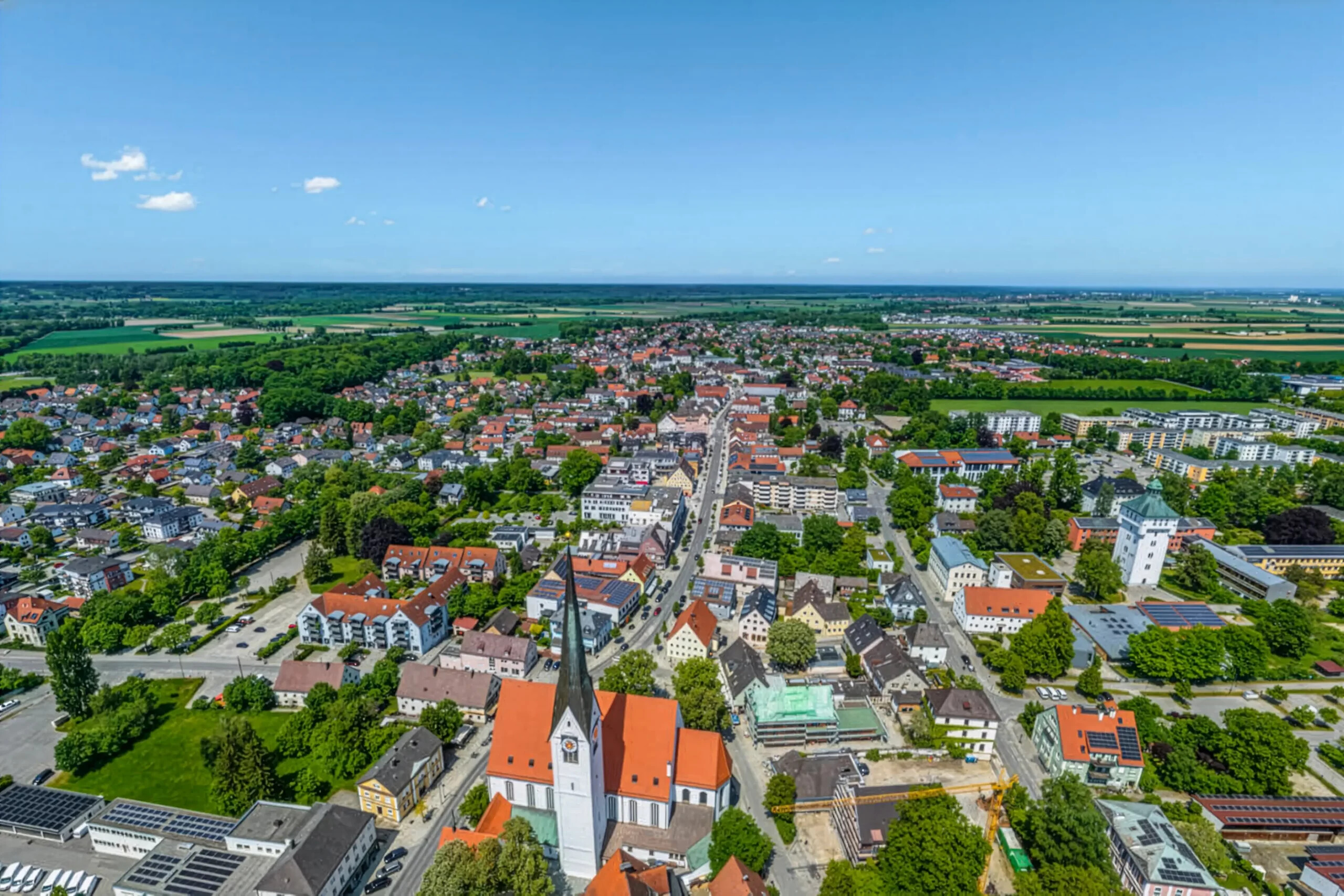Stadt Schwabmünchen mit Kirche, Häusern und Feldern unter blauem Himmel.