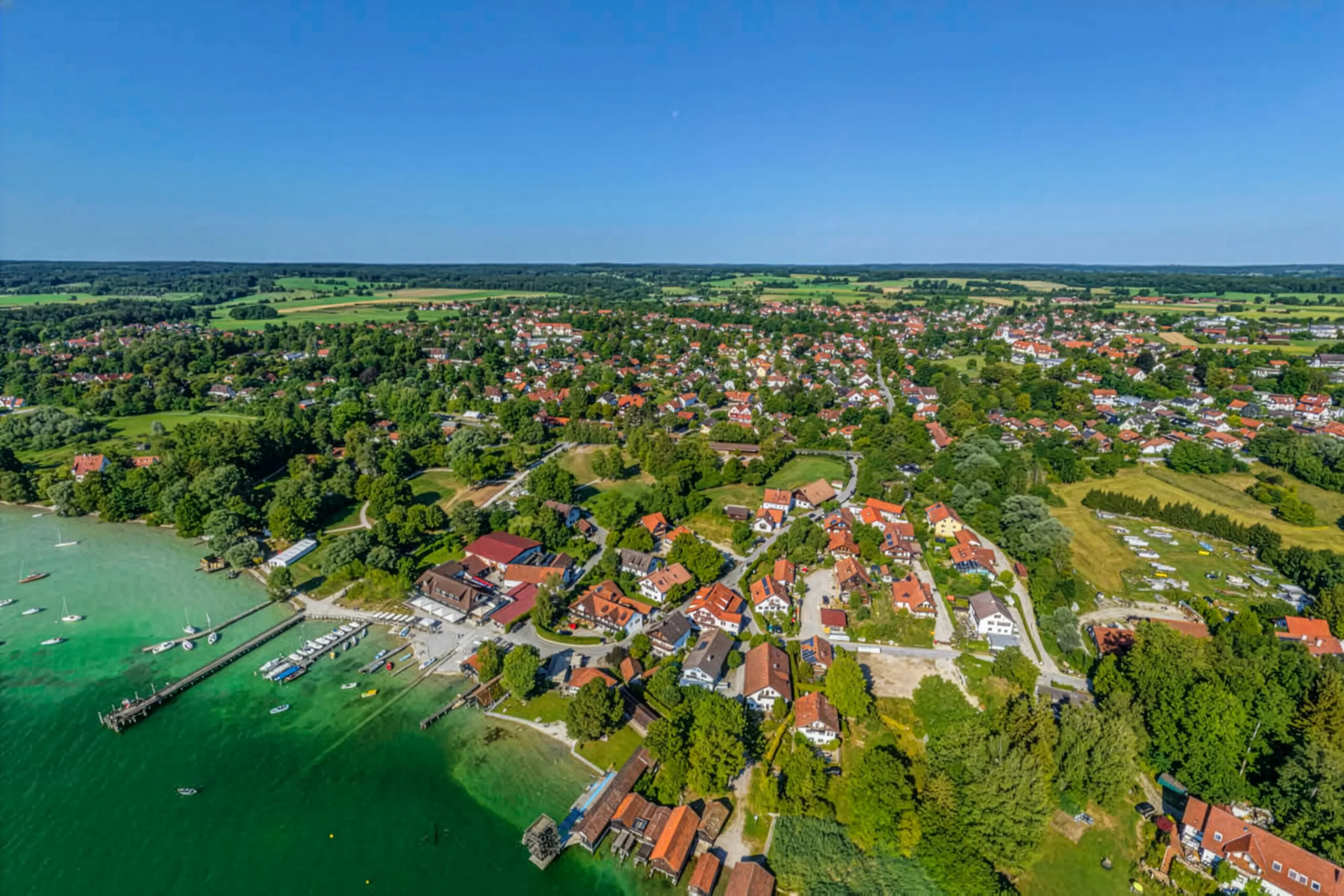 Utting am Ammersee, rote Dächer, Bäume, Docks, türkisfarbenes Wasser.