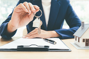 Mann mit Schlüssel über Klemmbrett und Hausmodel auf Tisch