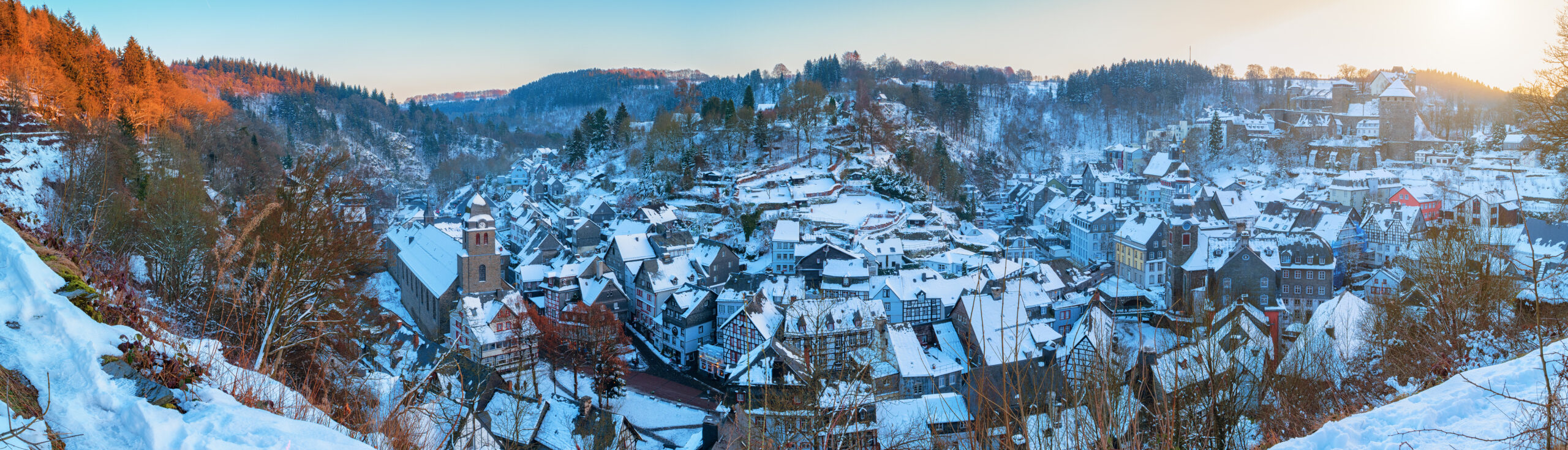 Verschneites Dorf zwischen bewaldeten Hügeln im Winter.