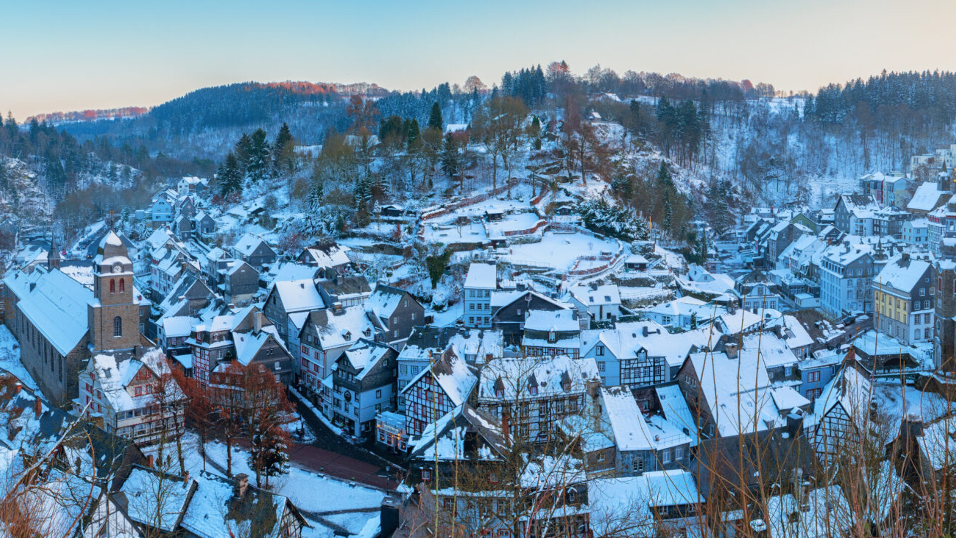Verschneites Dorf zwischen bewaldeten Hügeln im Winter.