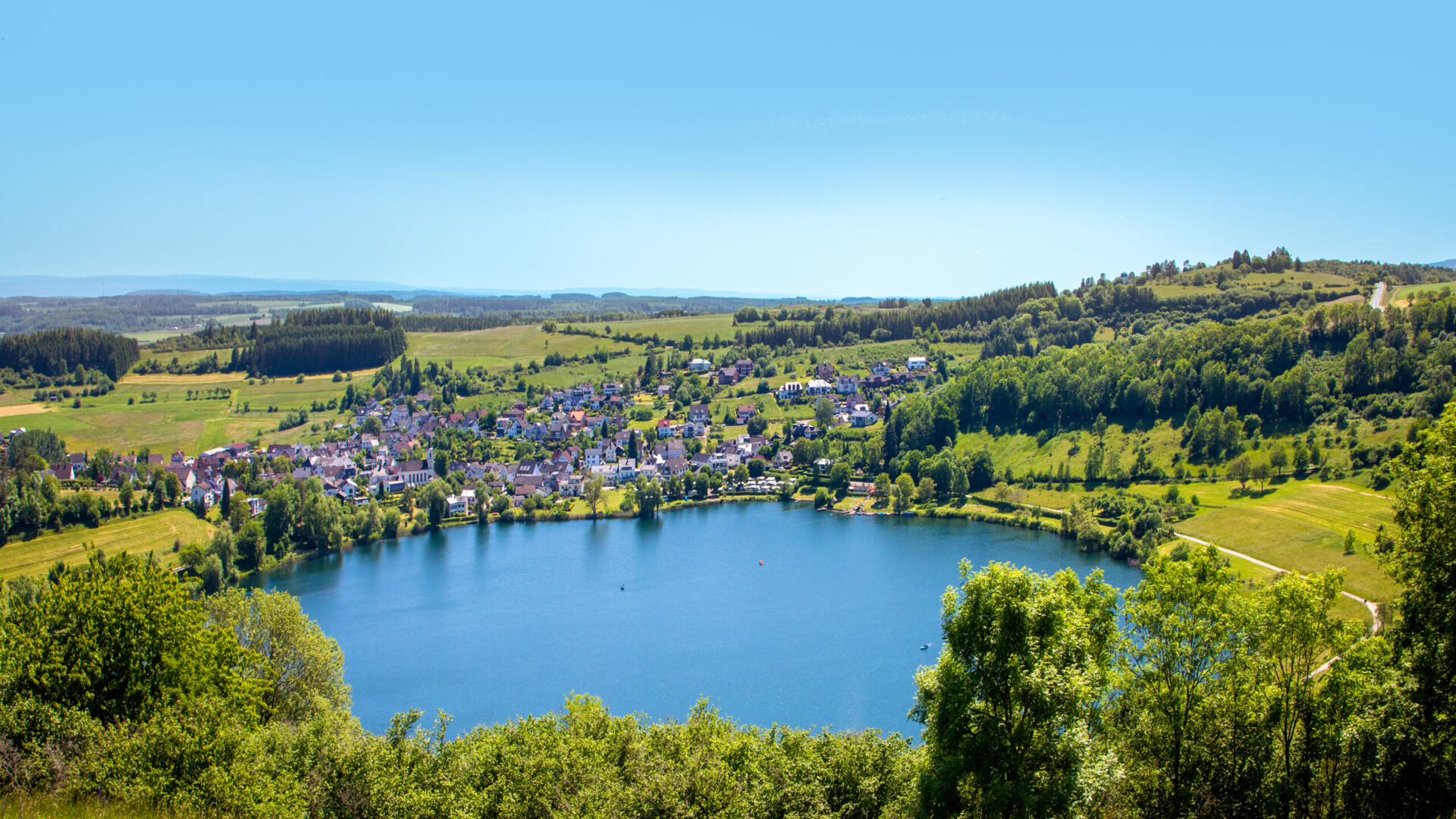 Kleinstadt an einem runden See mit Feldern und Bäumen.